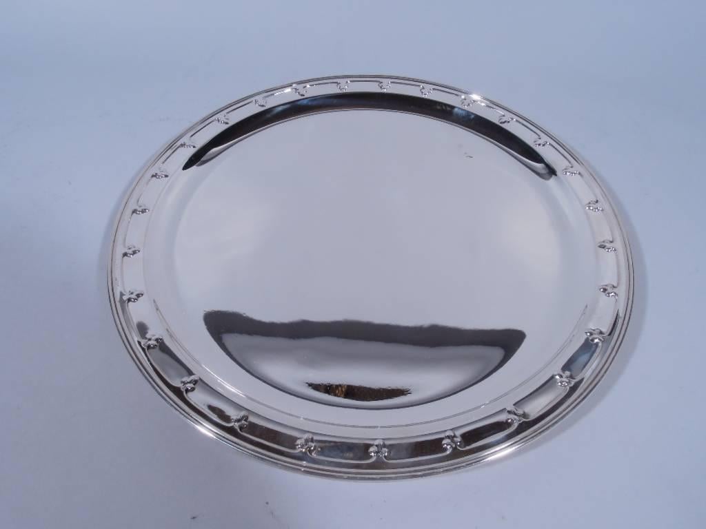 Sterling silver tray. Made by Tiffany & Co. in New York, circa 1911. Circular with well. Rim has applied band of stylized trefoils. Hallmark includes no. 18127A (first produced in 1911) and director’s letter m (1907-47). Very good