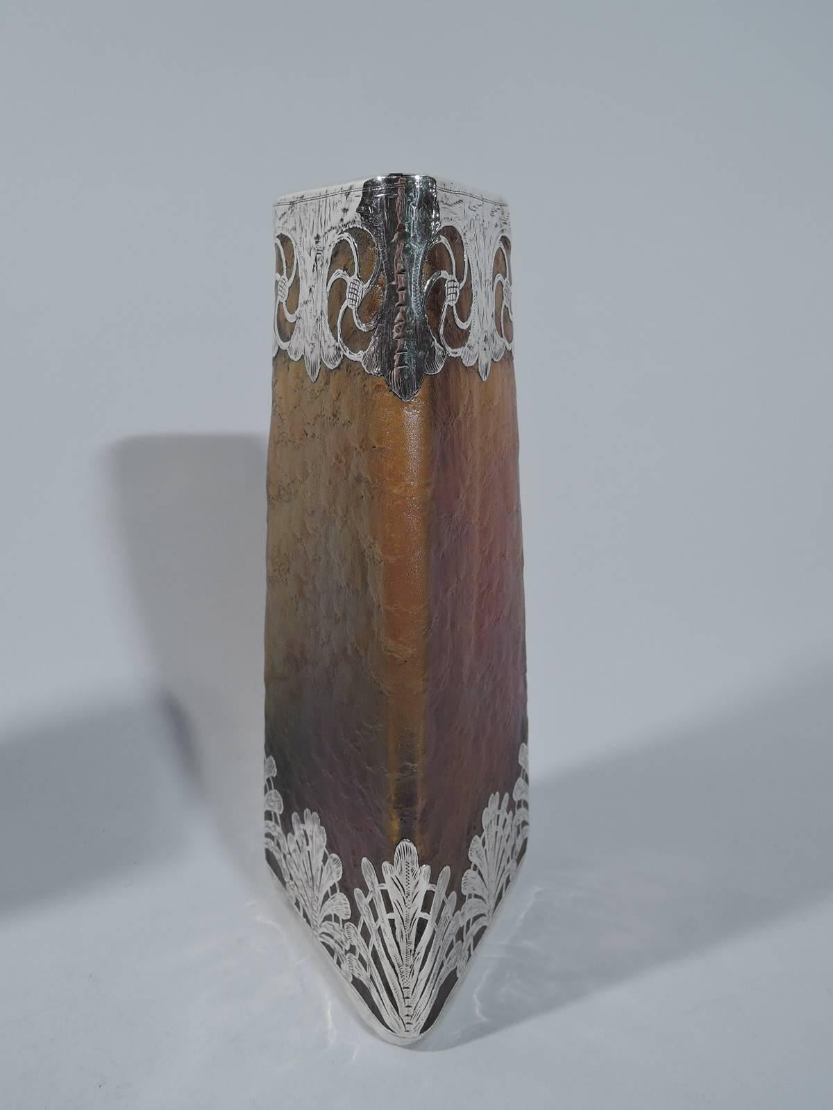 Pair of iridescent glass vases with silver overlay, ca 1900. Each: Three straight and upward tapering sides. The glass is thick and rusticated, and brownish in color. The base is overlaid with palmettes. The top is overlaid with rondels. Pontil