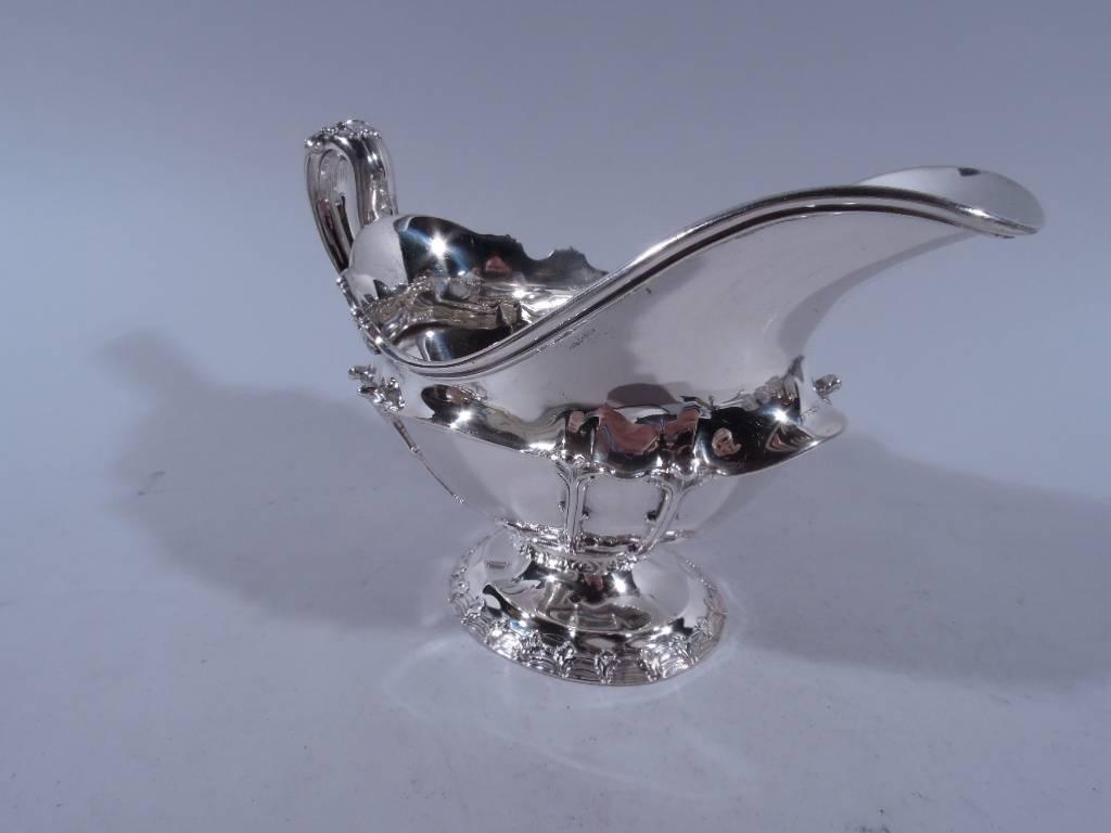 Fancy sterling silver gravy boat. Made by Tiffany & Co. in New York, circa 1902. Traditional form, high-looping handle with leaf cap and mounts and raised foot. Chased tendrils and scallop shells. Foot rim has scallop shells over wavy lines.