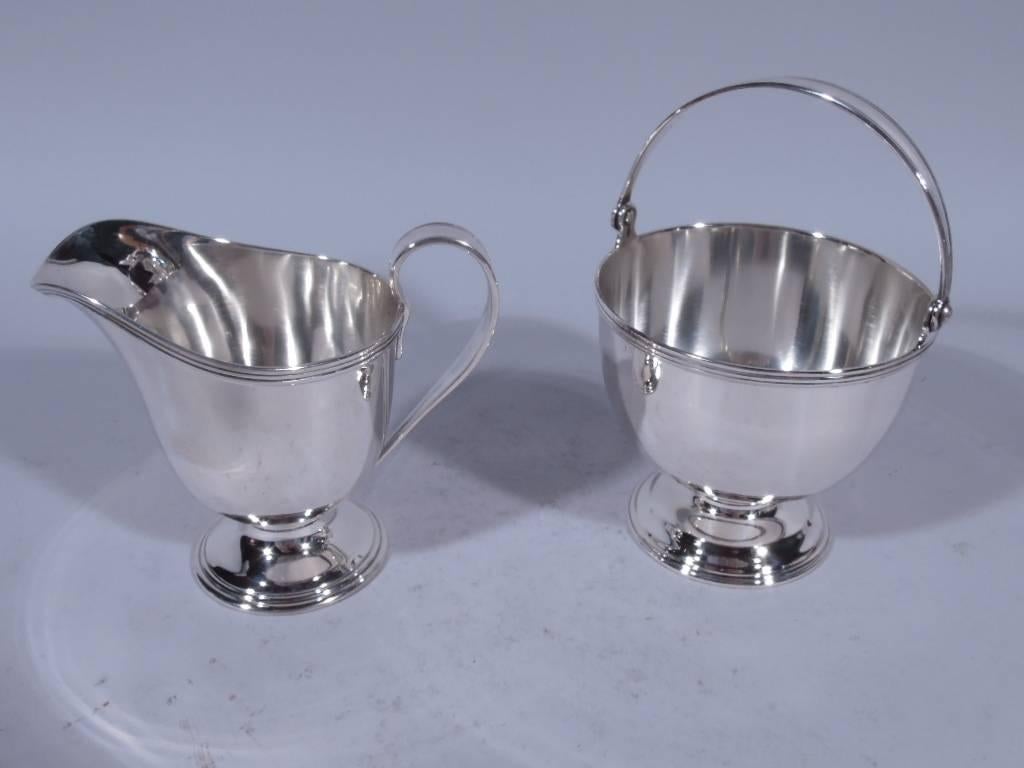 Sterling silver creamer and sugar. Made by Tiffany & Co. in New York, circa 1910. Creamer: helmet mouth with reeded rim, high looping scroll handle with incised bands, and stepped foot. Sugar: bowl has reeded rim and curved bottom, tapering swing