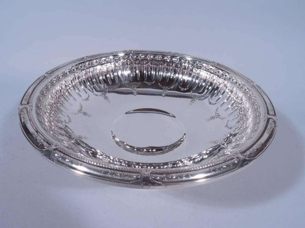 Pretty sterling silver footed bowl. Made by Gorham in Providence in 1926. Shallow and curved bowl with flat rim and short stepped foot. Chased and repousse stylized ornament with alternating lines and flowers joined by floral garlands. Rim has