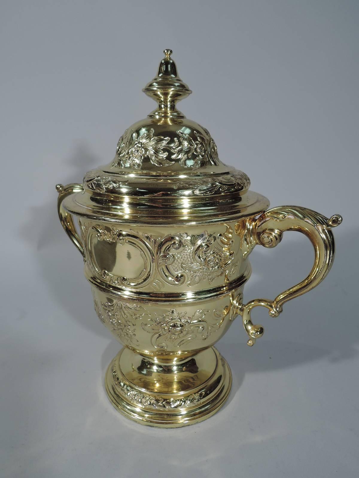 George V sterling silver trophy cup. Made by Edward Barnard & Sons in London in 1916. Ovoid body on raised foot, leaf-capped double-scroll side handles, and dome cover with finial. Chased and repousse flowers and scrolls and 2 scrolled cartouches