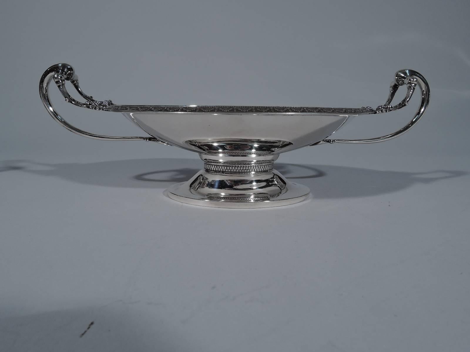 Sterling silver footed bowl. Made by Gorham in Providence in 1872. Shallow oval bowl with gently turned-down rim, and low-looping end handles split-mounted with volute scrolls and stylized leaves. Raised oval foot. Austere Greek Revival design