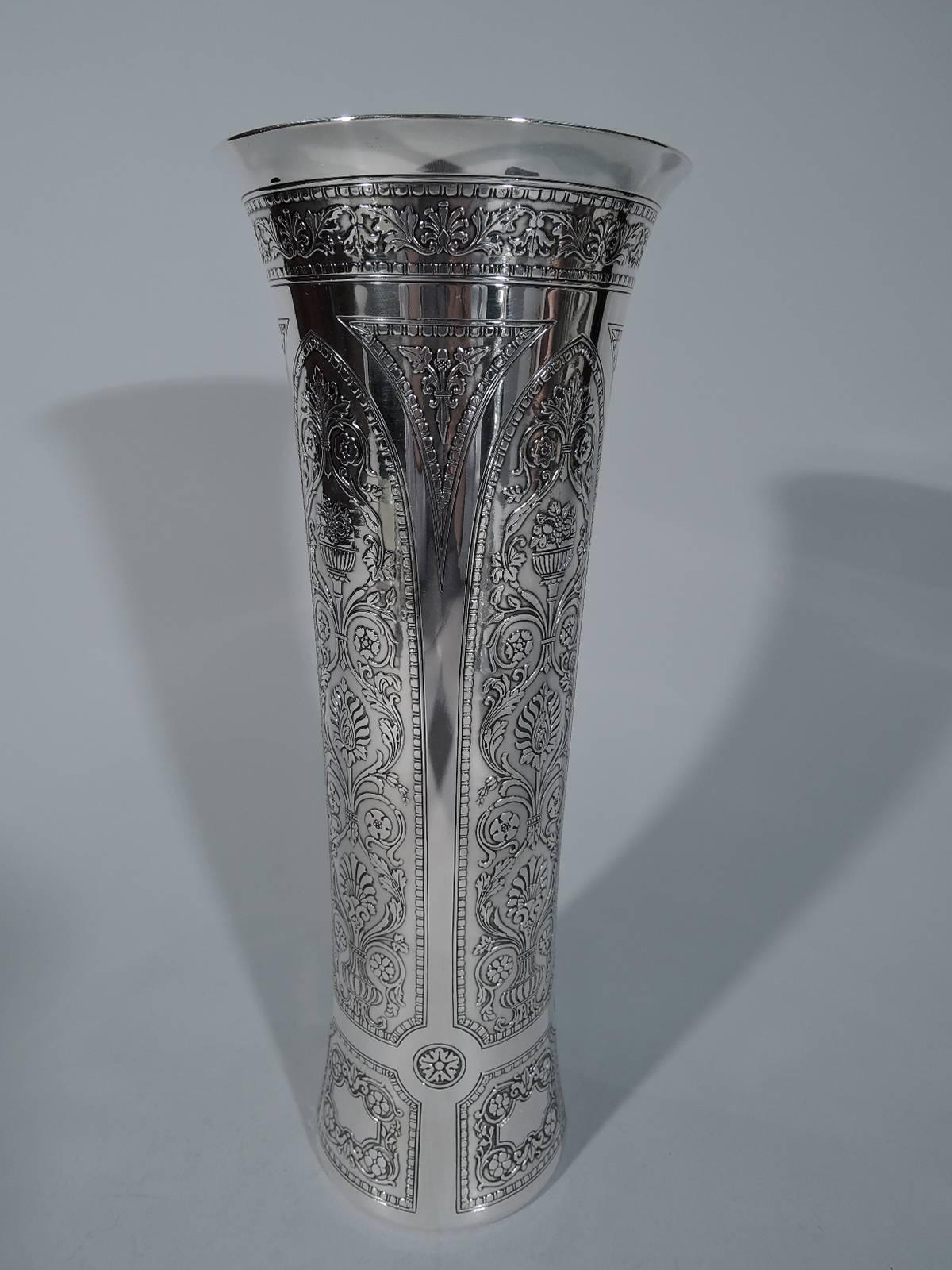 Sterling silver vase. Made by Tiffany & Co. in New York, circa 1912. Tapering cylinder with flared rim. Exterior has acid-etched frames with bead-and-reel borders and stylized vases, flowers, and leaves. A distinctive modernization of Edwardian