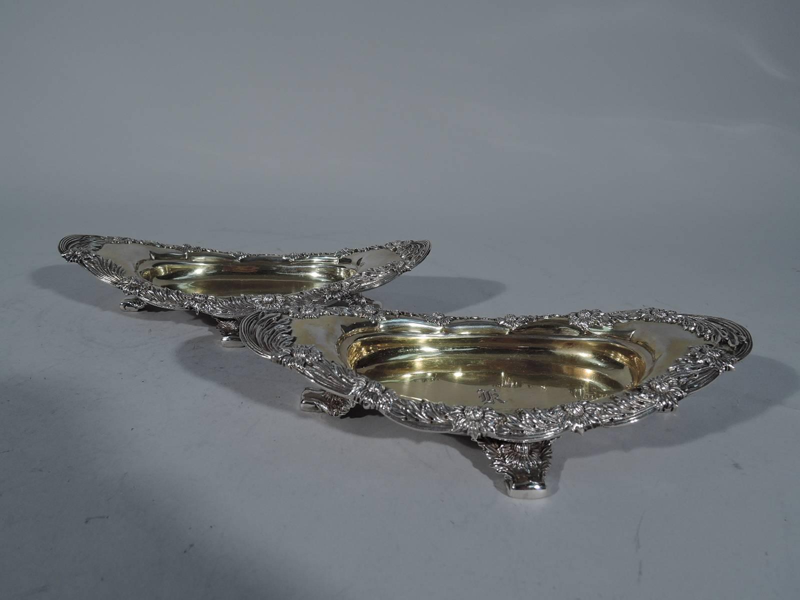 Pair of sterling silver bowls in Chrysanthemum pattern. Made by Tiffany & Co. in New York. Each: shallow oval well and oval rim with overhanding sides and elongated ends. Rests on four supports. A profusion of chrysanthemums on rim and supports.