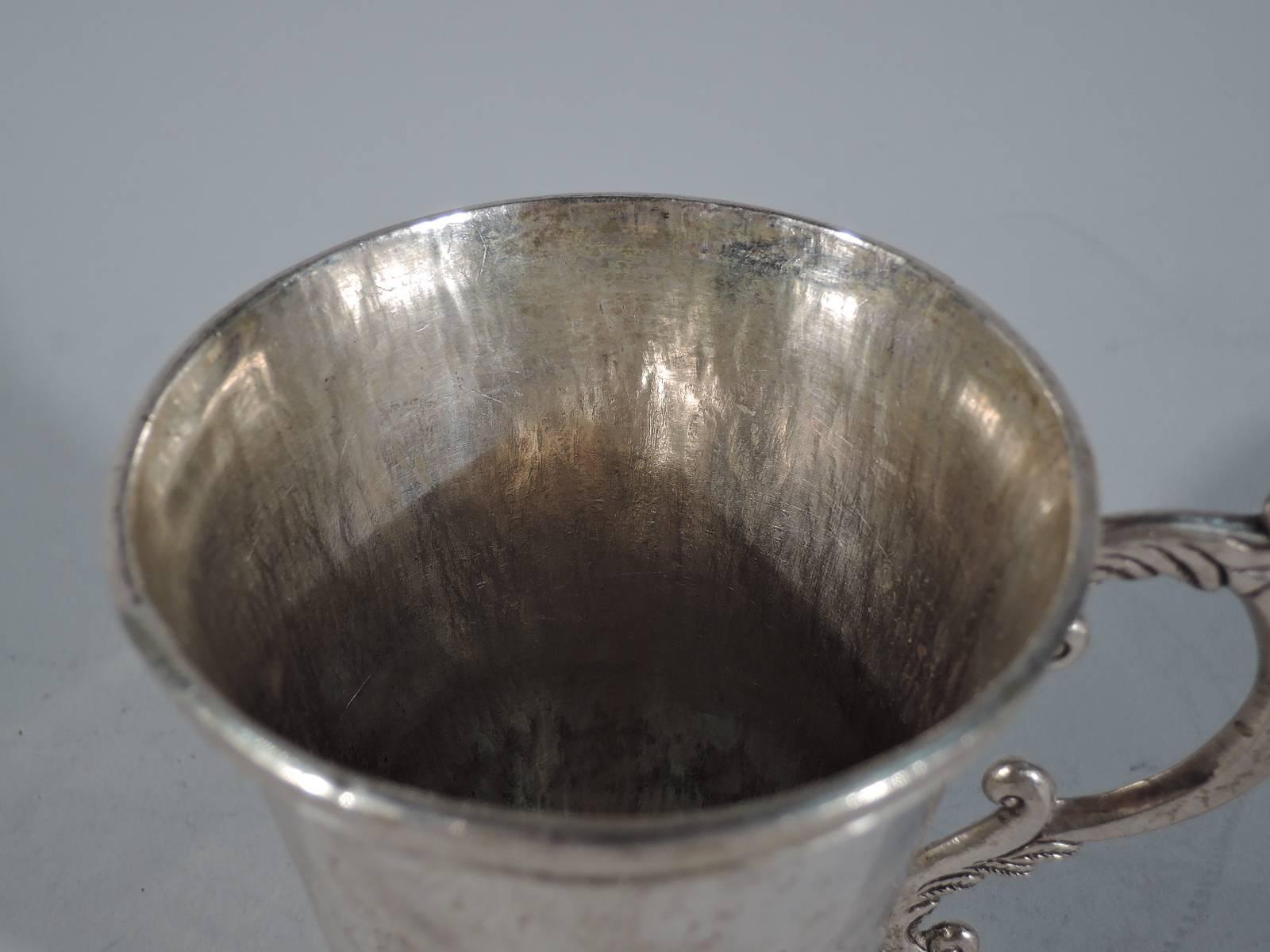 South American silver mug, circa 1850. Tapering sides and applied rim and foot. Engraved band with figures and flowers. A highlight is the man dangling upside down in a beast’s jaws and his spear-wielding rescuer. Worked s-scroll handle with leaf