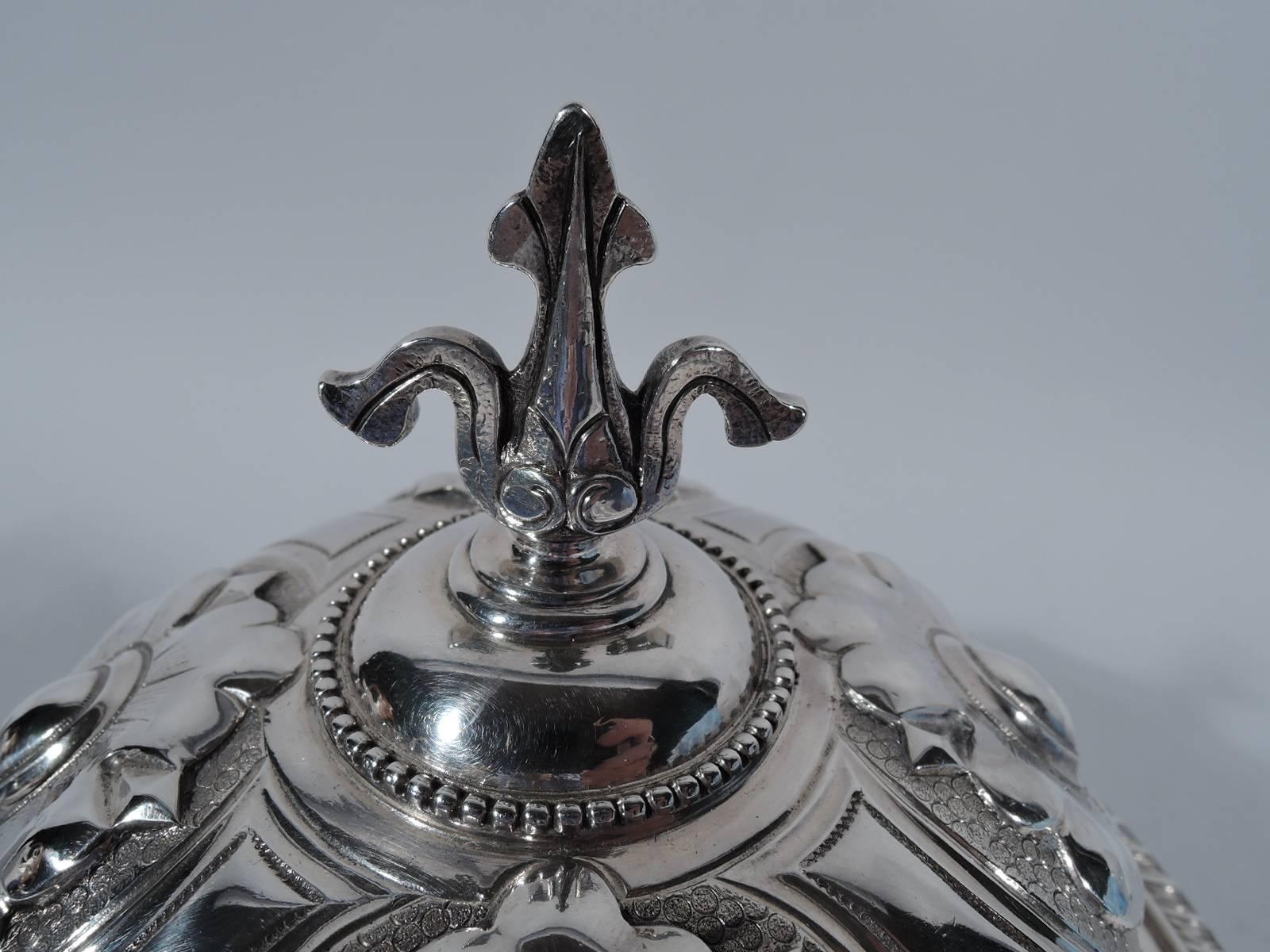 Early sterling silver covered butter dish. Made by Tiffany & Co. in in New York. Footed bowl with gadrooned rim. Domed cover with chased and repousse stylized blossoms on fish scale ground, beading and dentil, and fleur de lys finial. Four