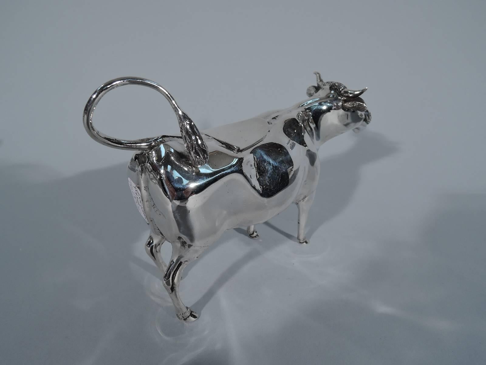 George V sterling silver cow creamer. Made in London in 1923. A beneficent bovine with stocky body, pointy horns and flexed ears. Sweet expression with gaping mouth and red glass eyes. Hinged back flap and ring handle in form of flicked-back tail.