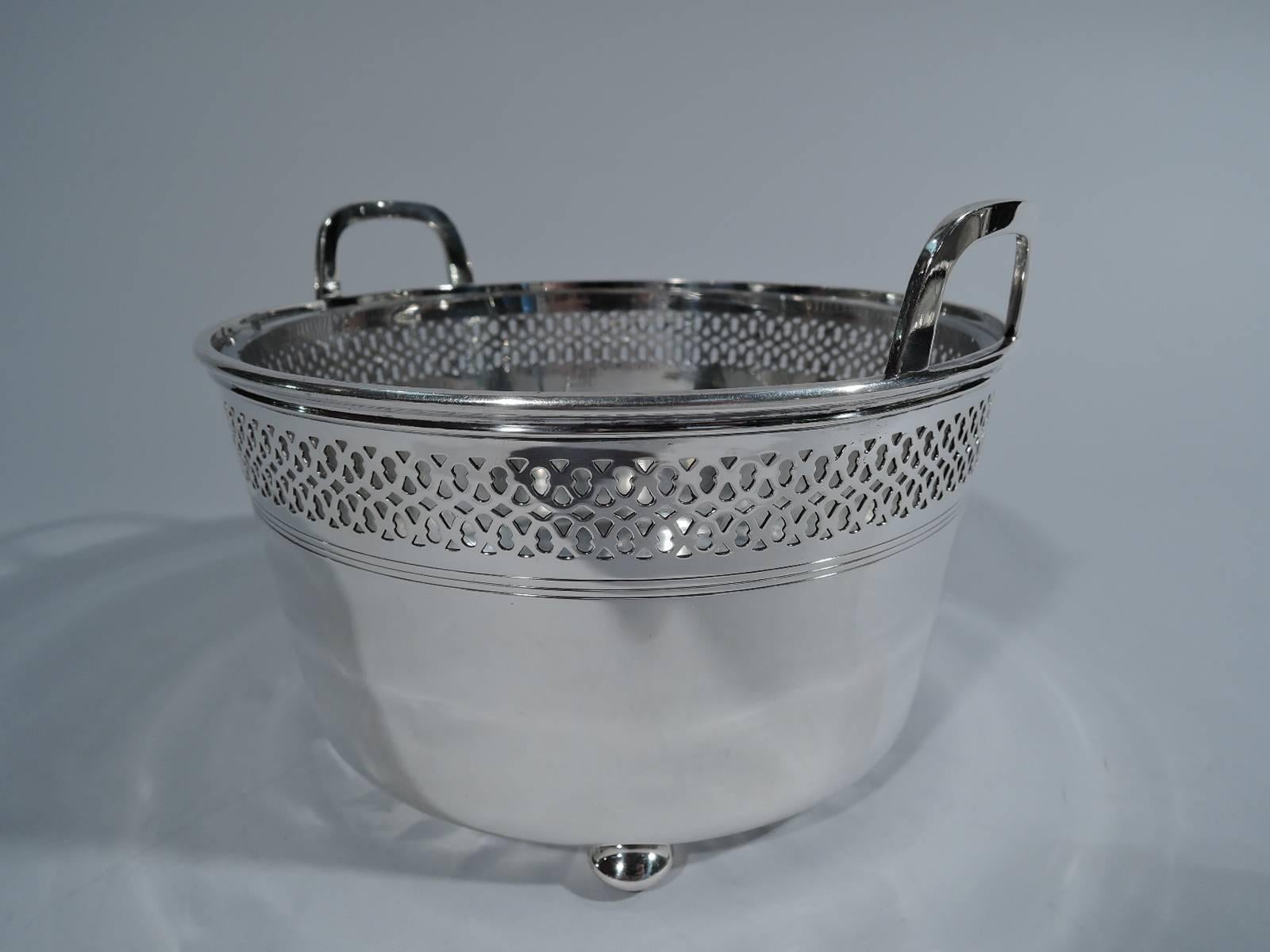 Edwardian sterling silver ice bucket. Made by Tiffany & Co. in New York, circa 1908. Straight and tapering sides, bracket handles mounted to rim, and four ball supports. Pierced interlacing and incised banding. Detachable clear glass liner with star