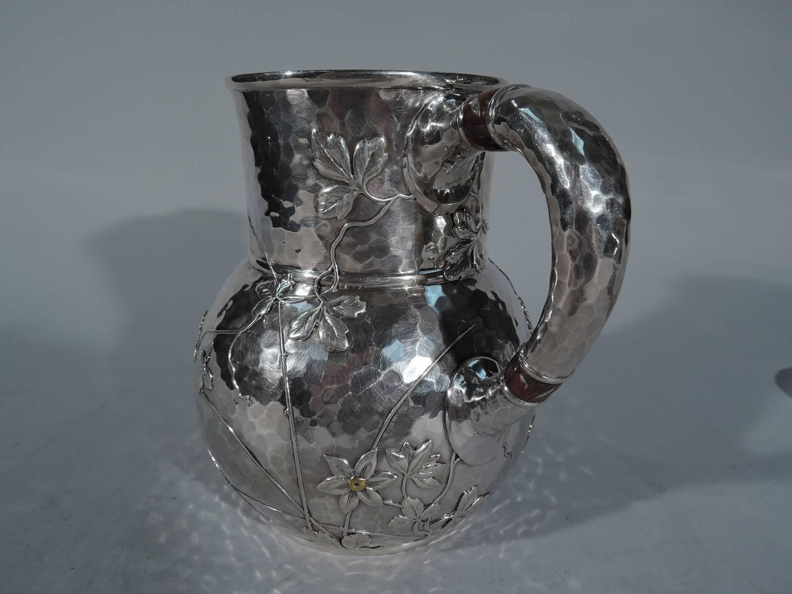 Wasserkrug aus Sterlingsilber und Mischmetall. Hergestellt von Tiffany & Co. in New York, ca. 1885. Kugelförmiger Korpus, gerader Hals und C-Schneckengriff. Ganzflächige wabenförmige Handhämmerung. Aufgetragene Blüten, Blattranken und