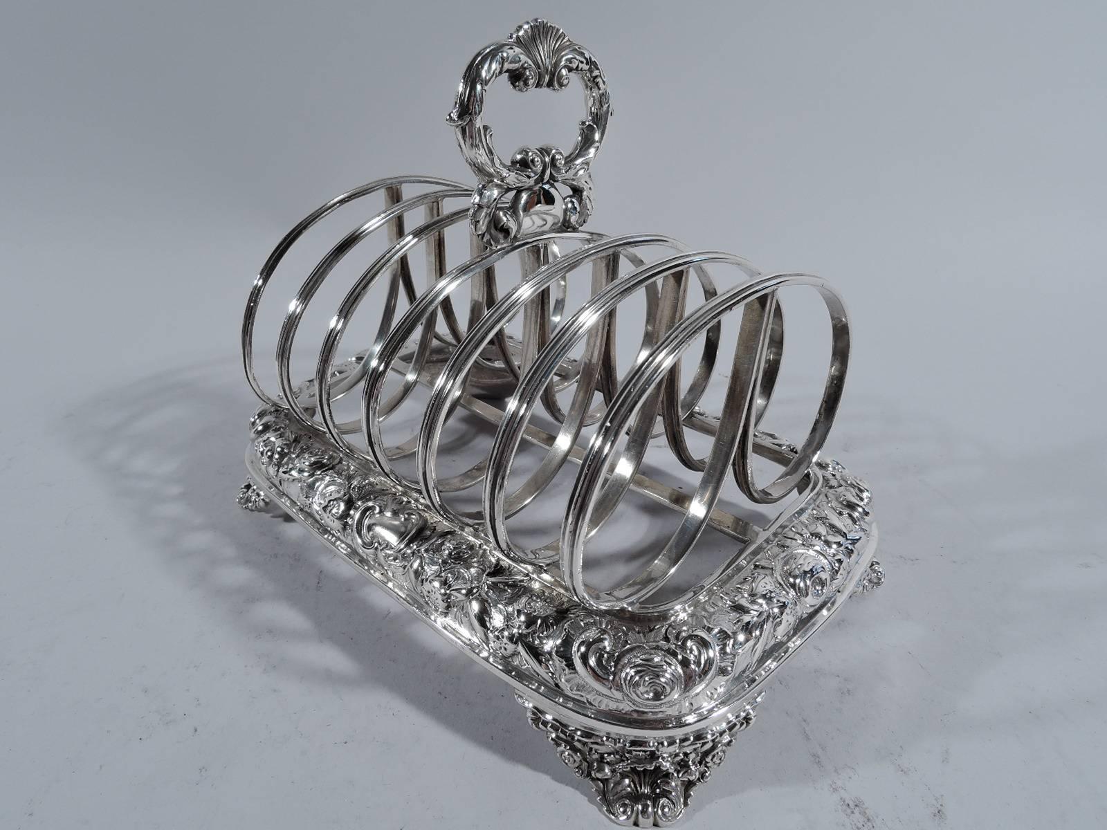 George IV sterling silver toast rack. Made by Joseph Craddock in London in 1826. Seven partitions in form of reeded double loops mounted to quadrilateral frame on corner supports with volute scrolls and flowers. Frame has central stretcher and