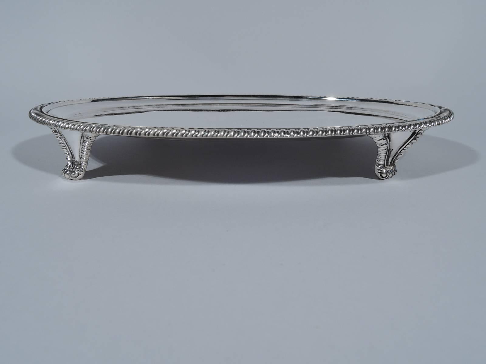 Georgian-style sterling silver salver. Made by Daniel & John Wellby in London in 1910. Oval with gadrooned rim. Rests on four tapering and gadrooned supports terminating in split volute scrolls. Hallmarked. Weight: 20 troy ounces.