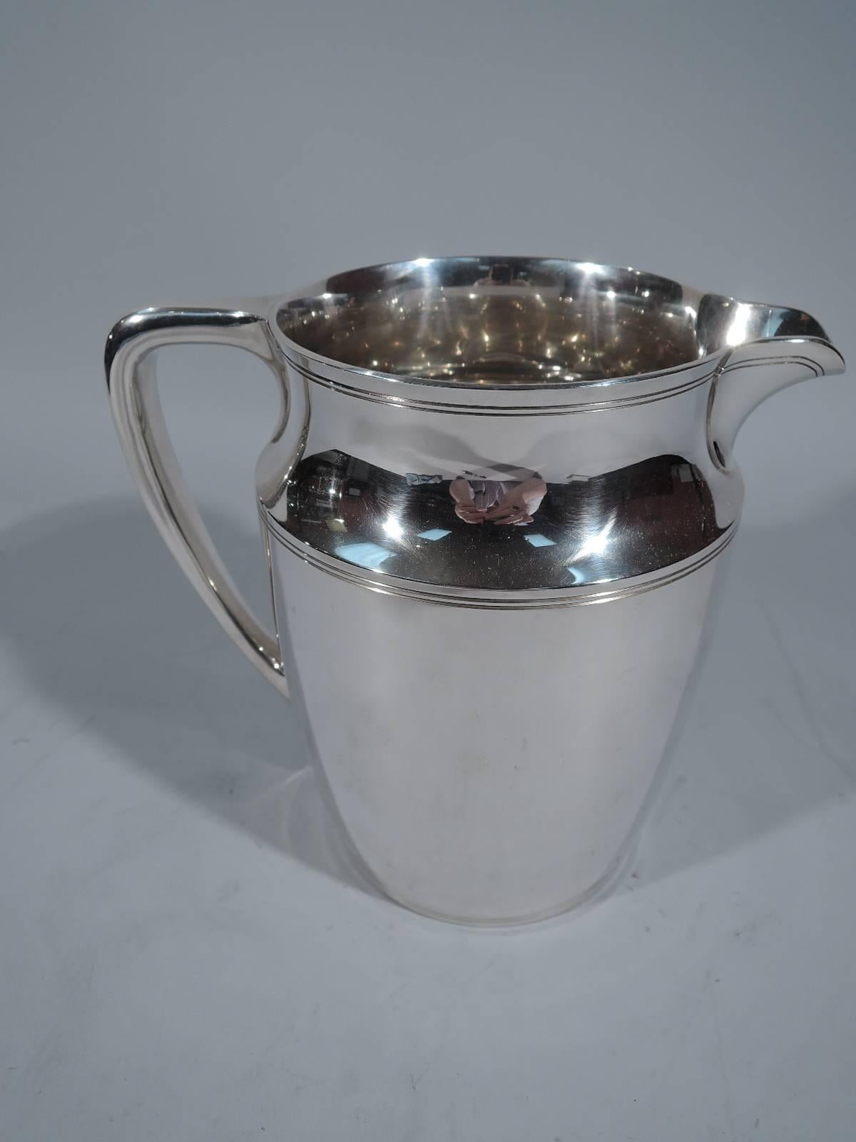 Sterling silver water pitcher. Made by Tiffany & Co. in New York. Gently curved and tapering sides, inset neck, and scroll bracket handle. Double linear bands incised at shoulder and rim. Holds 4 1/4 pints. Hallmark includes pattern no. 20211,
