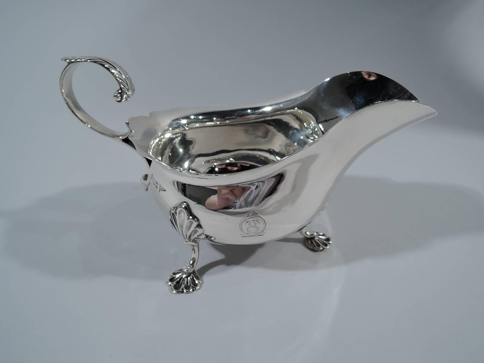 George V sterling silver gravy boat. Made by Walker & Hall in Sheffield in 1912. Wide curved body with leaf-capped double-scroll handle and three scallop shell-mounted supports. Armorial engraved on one side. A nice Georgian-style piece. Hallmark