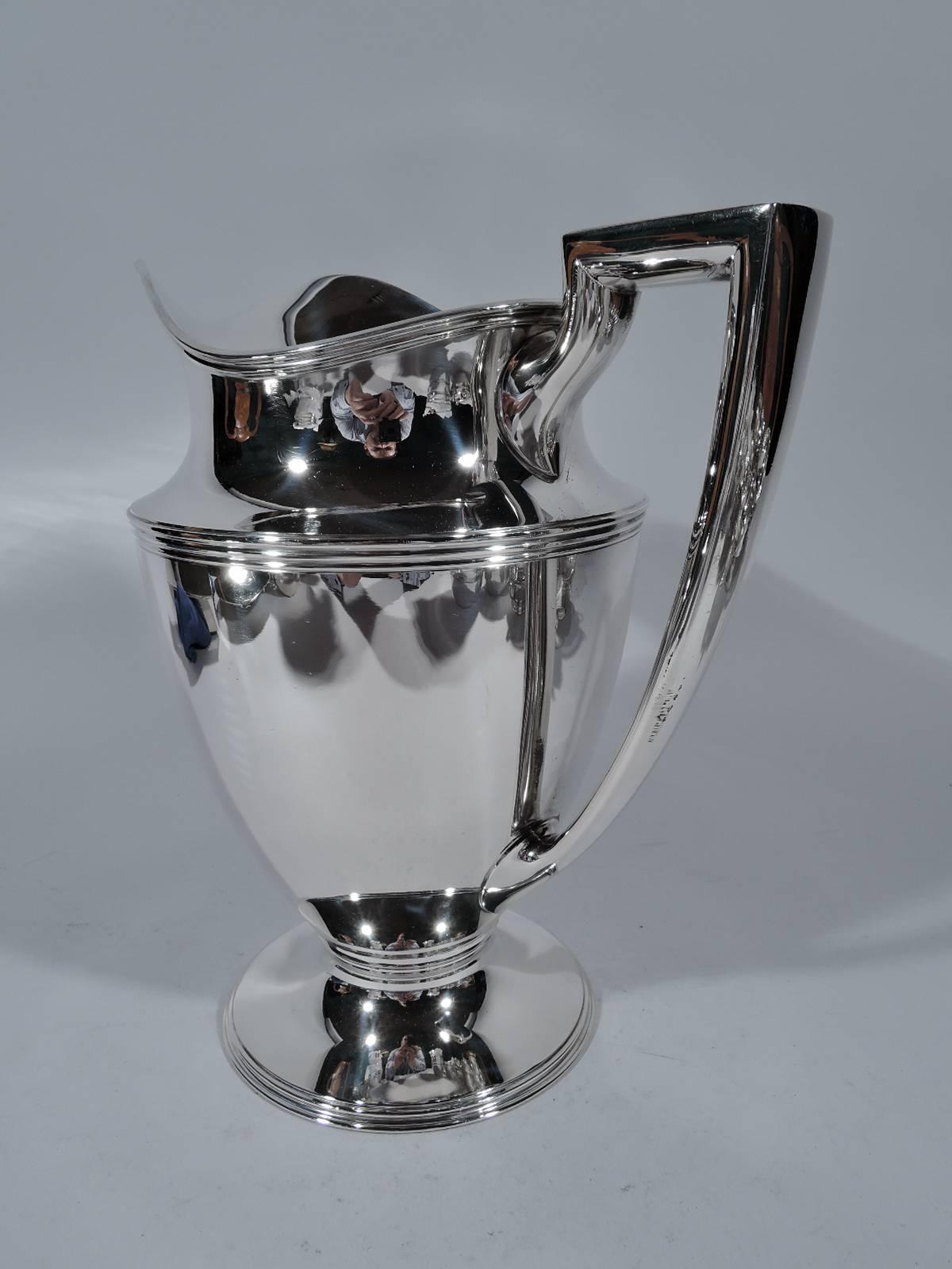 Sterling silver water pitcher. Made by Tiffany & Co. in New York. Curved and tapering body, raised and stepped foot, scrolled bracket handle, and helmet mouth. Ornamental reeding. Hallmark includes pattern no. 18181, director’s letter m (1907-1947),