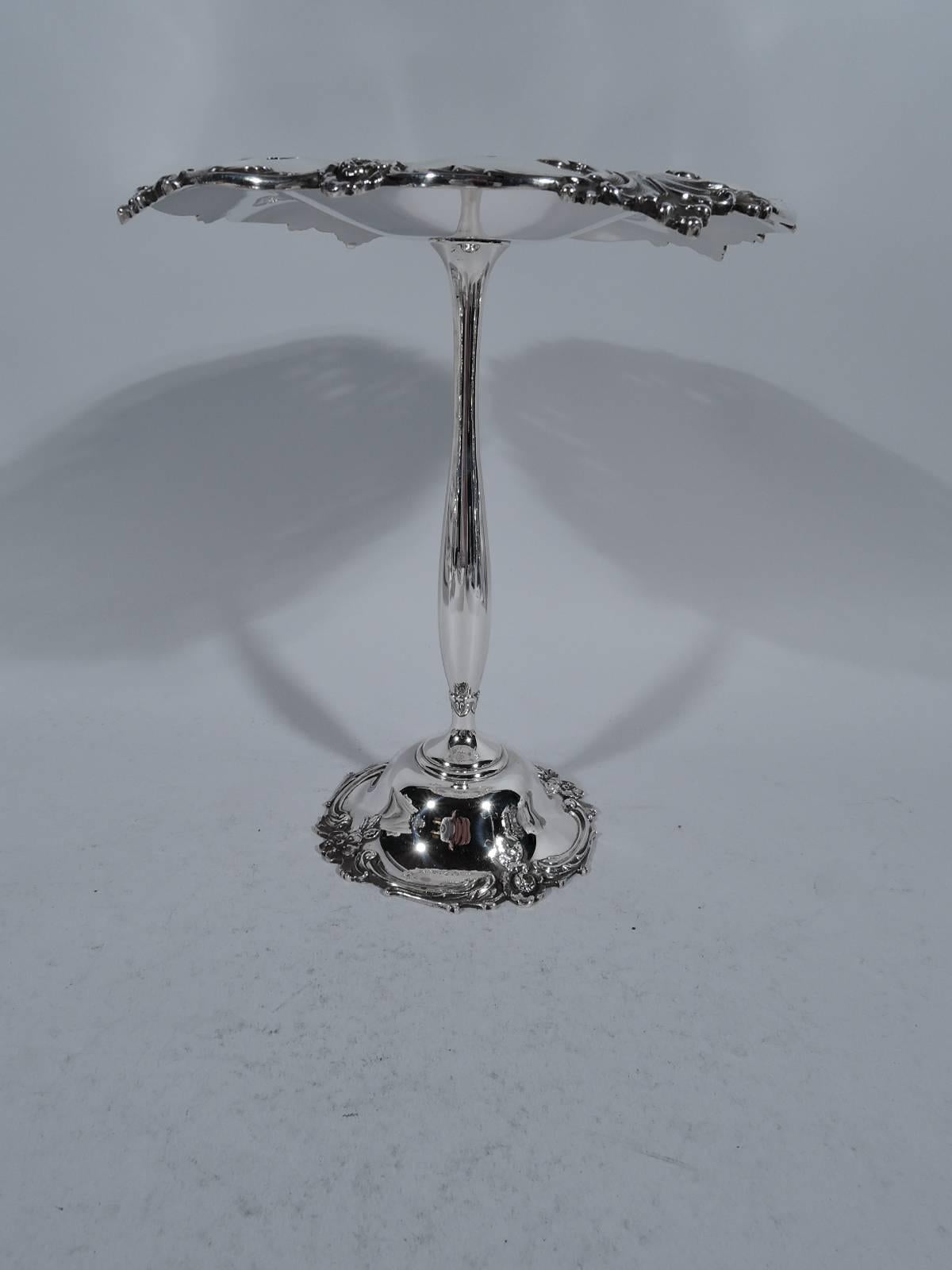 Sterling silver compote. Made by Tiffany & Co. in New York. Shallow bowl, thin baluster shaft, and dome foot. Scrolled rims with leaves and flowers. Bowl has discreet piercing. Traditional ornament on an unusual (that is, tall) form. Hallmark