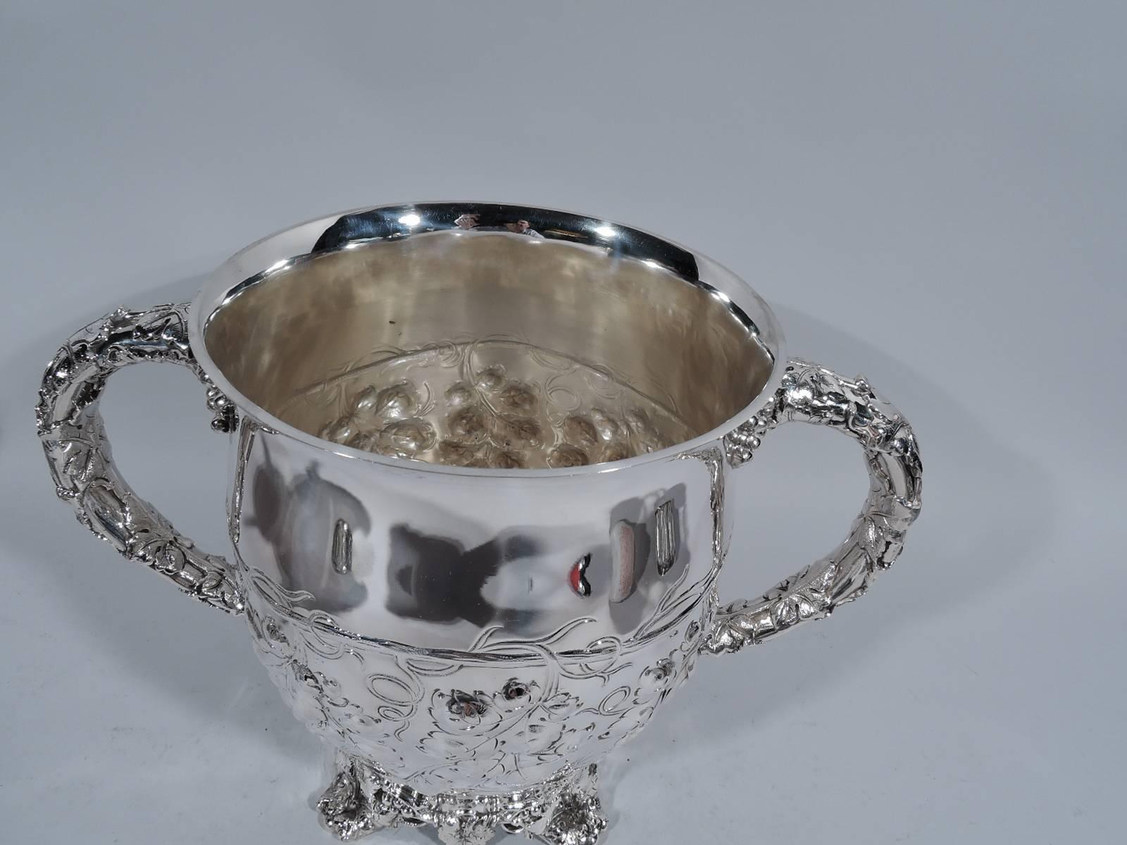 Sterling silver trophy cup. Made by Dominick & Haff in New York, circa 1890. Curved sides with c-scroll side handles. Raised foot with 4 leaf supports. Body and foot encircled with fruiting grapevines. Handles have applied leaves with grape bunch