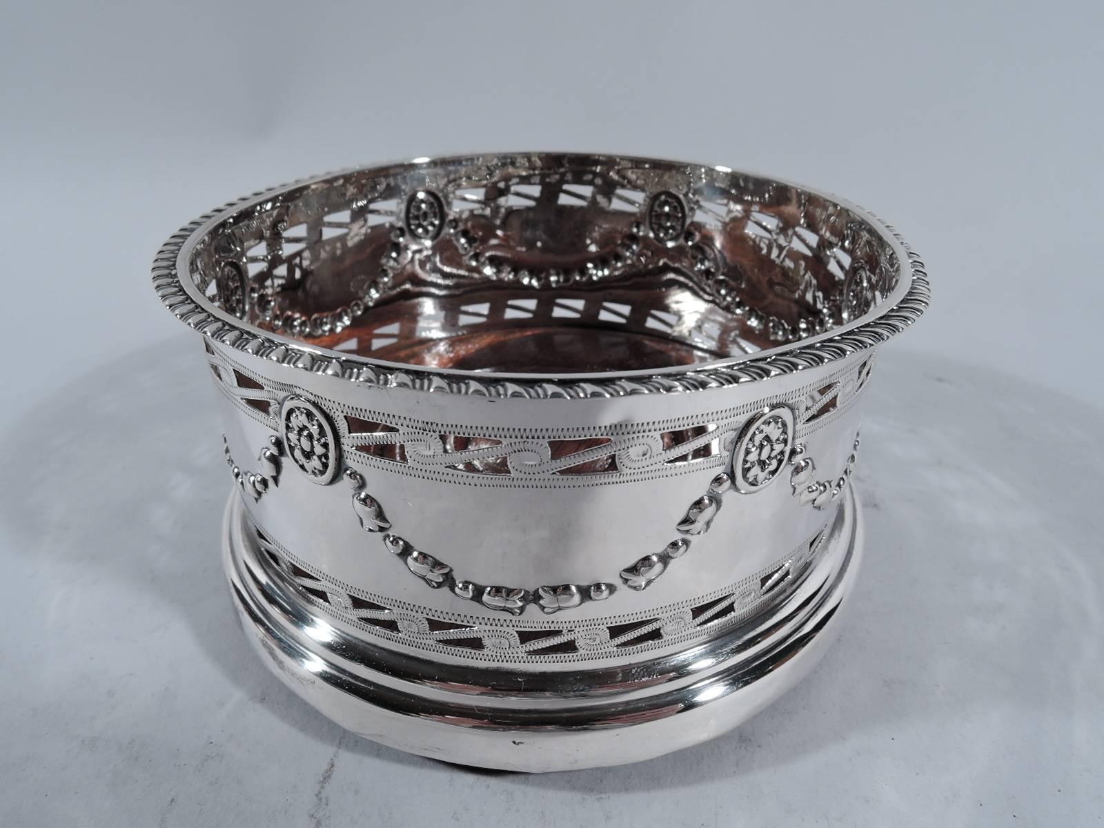 Edwardian sterling silver wine bottle coaster. Made by George Nathan and Ridley Hayes in Chester in 1905. Repousse garland with paterae between two bands of pierced Vitruvian scroll. Gadrooned rim. Stained-wood and felt-lined well. A charming and