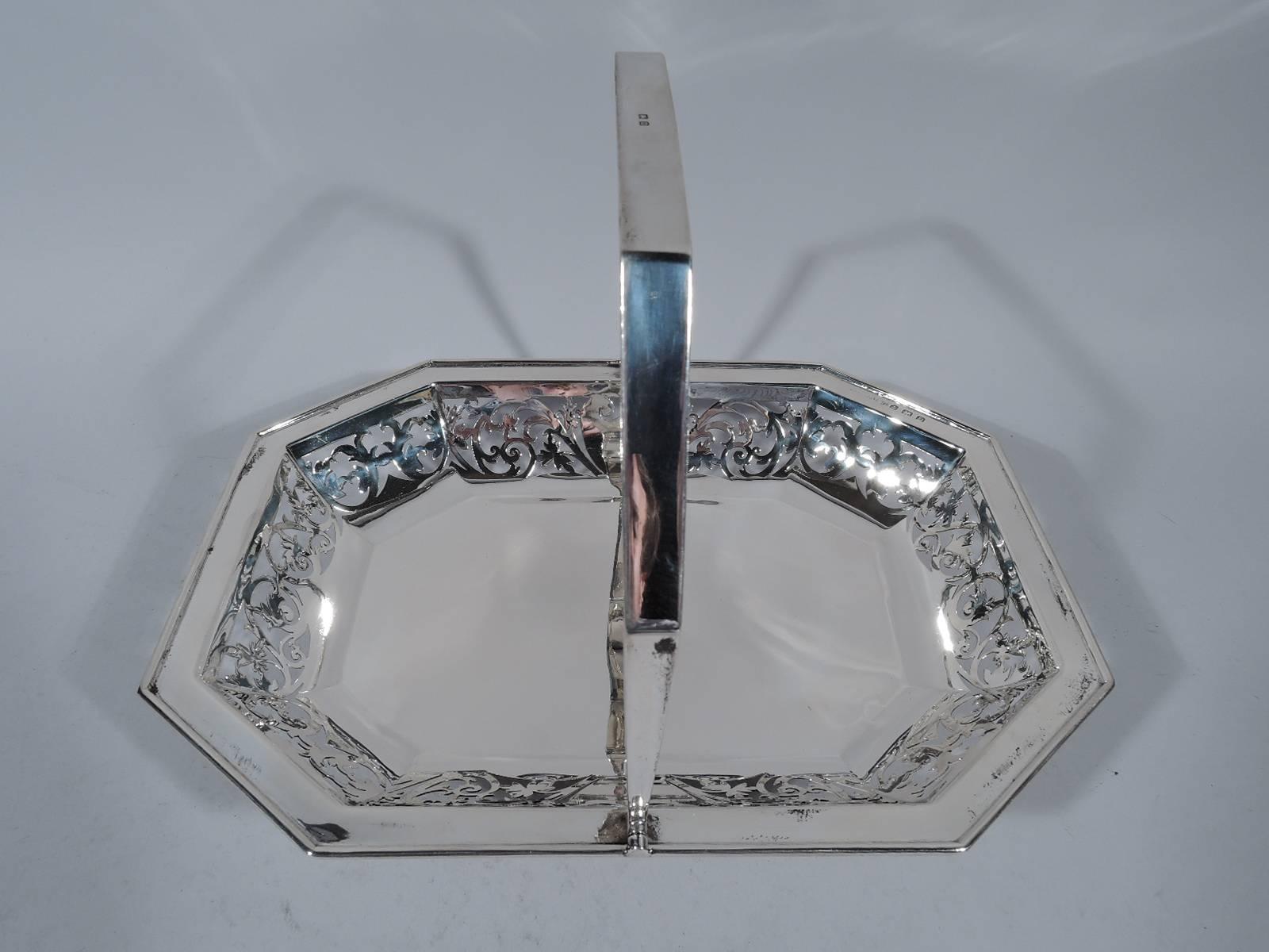 George V sterling silver basket. Made by Joseph Gloster in Birmingham in 1928. Rectangular with chamfered corners, solid well, tapering sides, flat molded rim, and chamfered swing handle. Sides have pierced semi-abstract scroll pattern and two solid