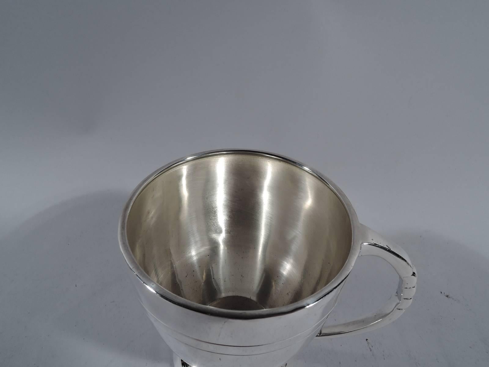 Elizabeth II sterling silver baby cup. Made by John B. Chatterley & Sons in Birmingham in 1960. Curved and tapering bowl on raised foot. Notched C-scroll handle. Incised double bands at top and bottom. Hallmarked. Measure: Weight 3.3 troy ounces.