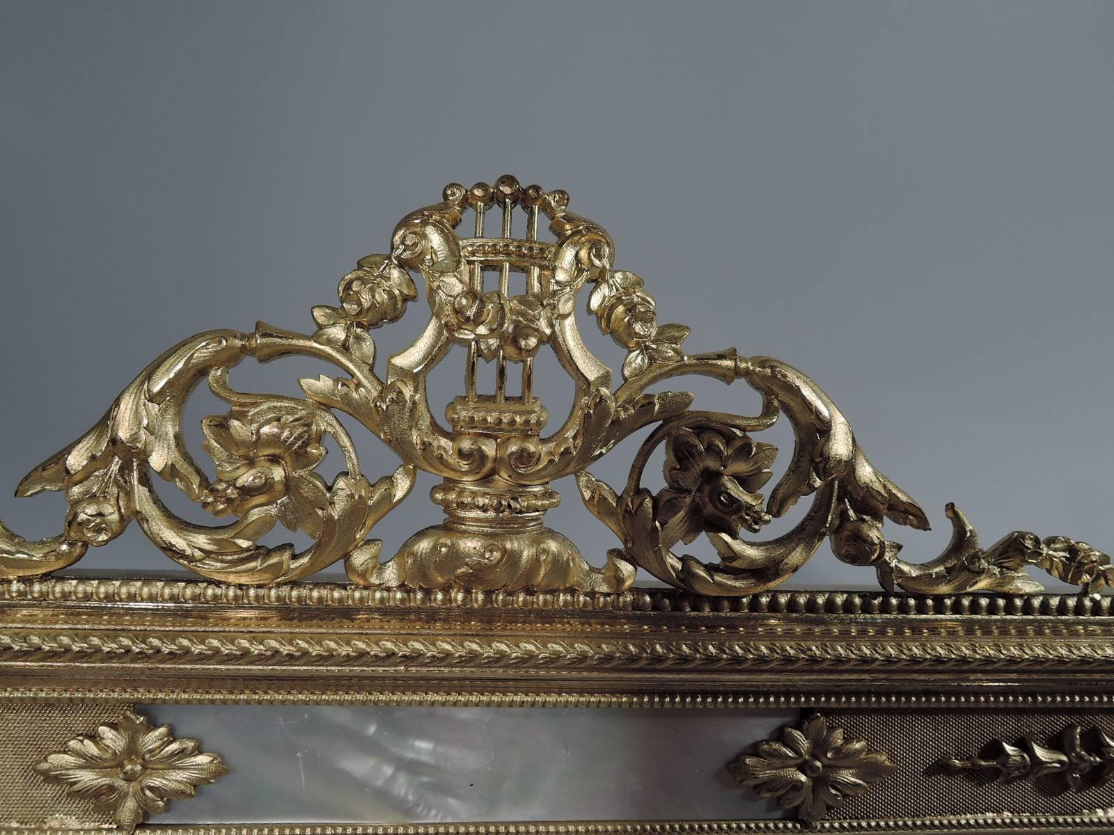 Antique French gilt bronze and mother of pearl picture frame. Rectangular window bordered by red velvet in turn bordered by gilt bronze and mother of pearl with applied scrolls and leaves. Pierced pediment in form of lyre and rinceaux. With glass,