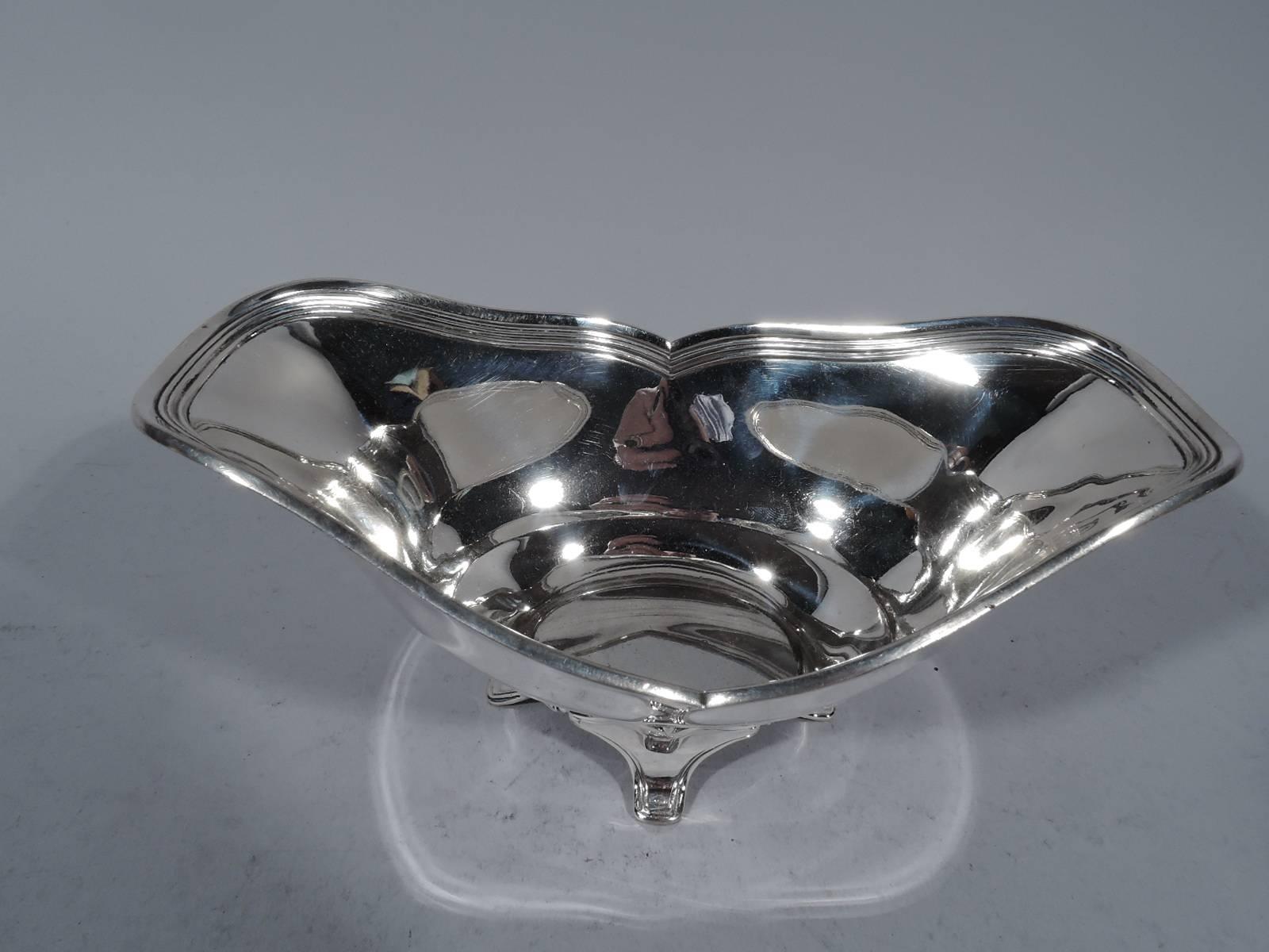 Sterling silver bowl. Made by Tiffany & Co. in New York, circa 1910. Asymmetrical rim with interior reeding. Sides crimped at center. Rests on four supports with scrolled mounts. Hallmark includes pattern no. 15602E1 and director’s letter m