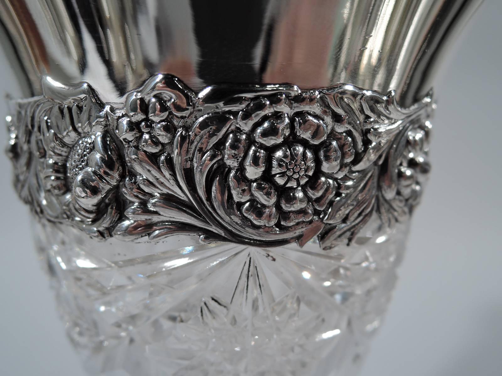 Brilliant-cut-glass vase with sterling silver collar. Made by Tiffany & Co. in New York, circa 1910. Fluted and waisted with cut notches, stars, and diaper pattern. Collar has flared rim with repousse flowers. Hallmark includes director’s letter m,