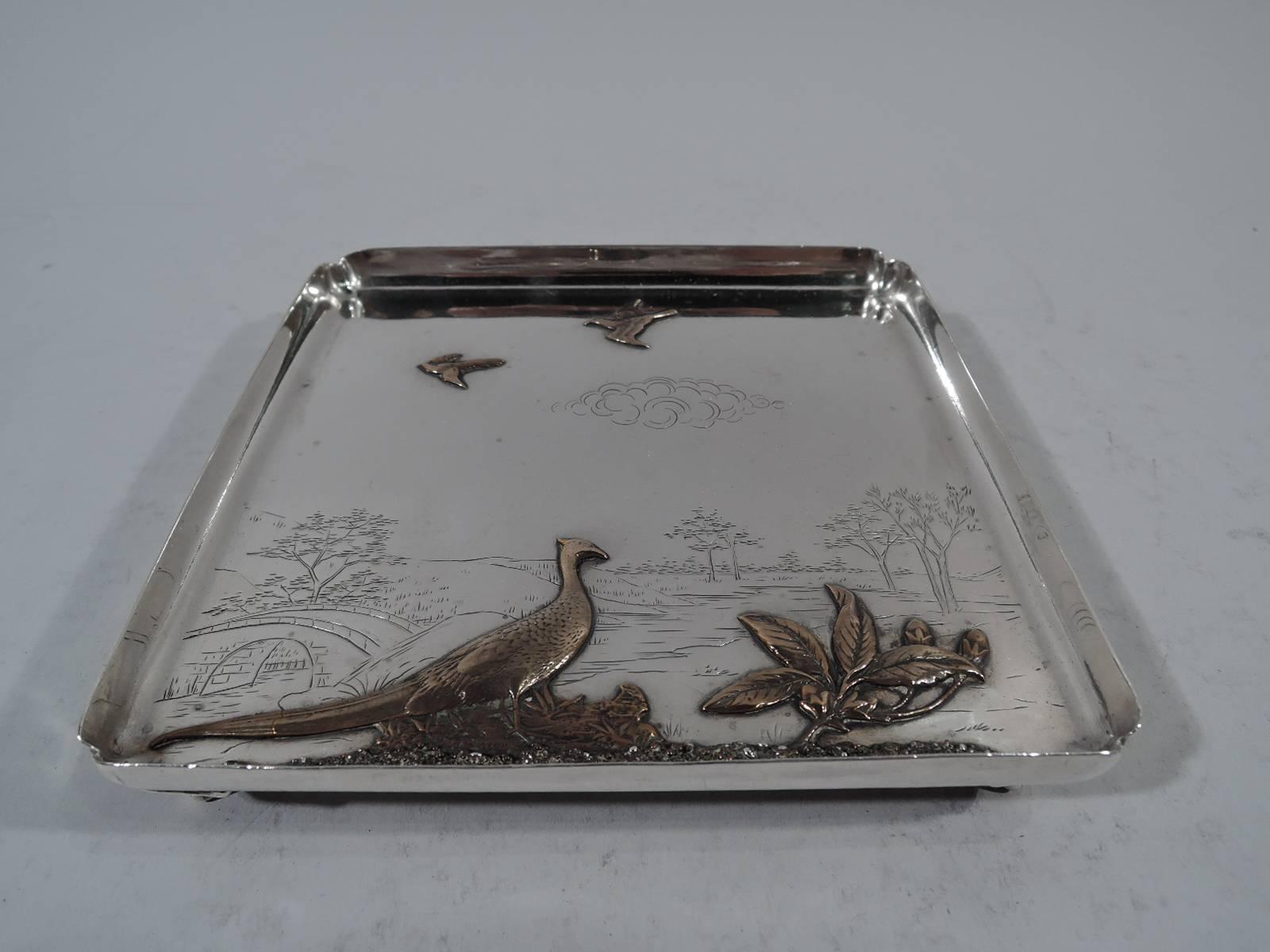 Mixed metal and sterling silver landscape salver. Made by Gorham in Providence in 1881. Square with gently tapering sides and crimped corners with pierced volute scroll supports. Engraved landscape with trees, hills, and stone bridge. In foreground