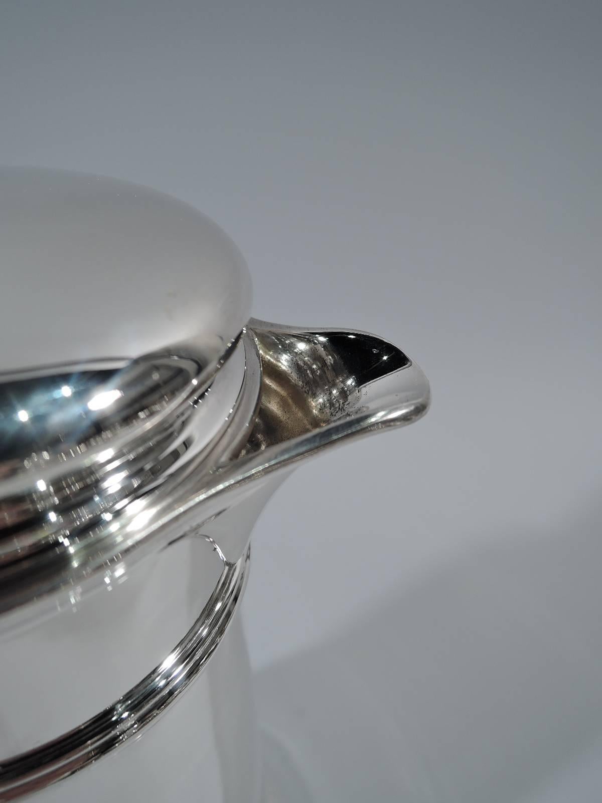 Art Deco sterling silver cocktail shaker. Made by Tiffany & Co. in New York, circa 1931. Conical with scroll bracket handle and v-spout. Bun cover with built-in strainer. Molded bands near top and at base. Spare and functional barware. Hallmark