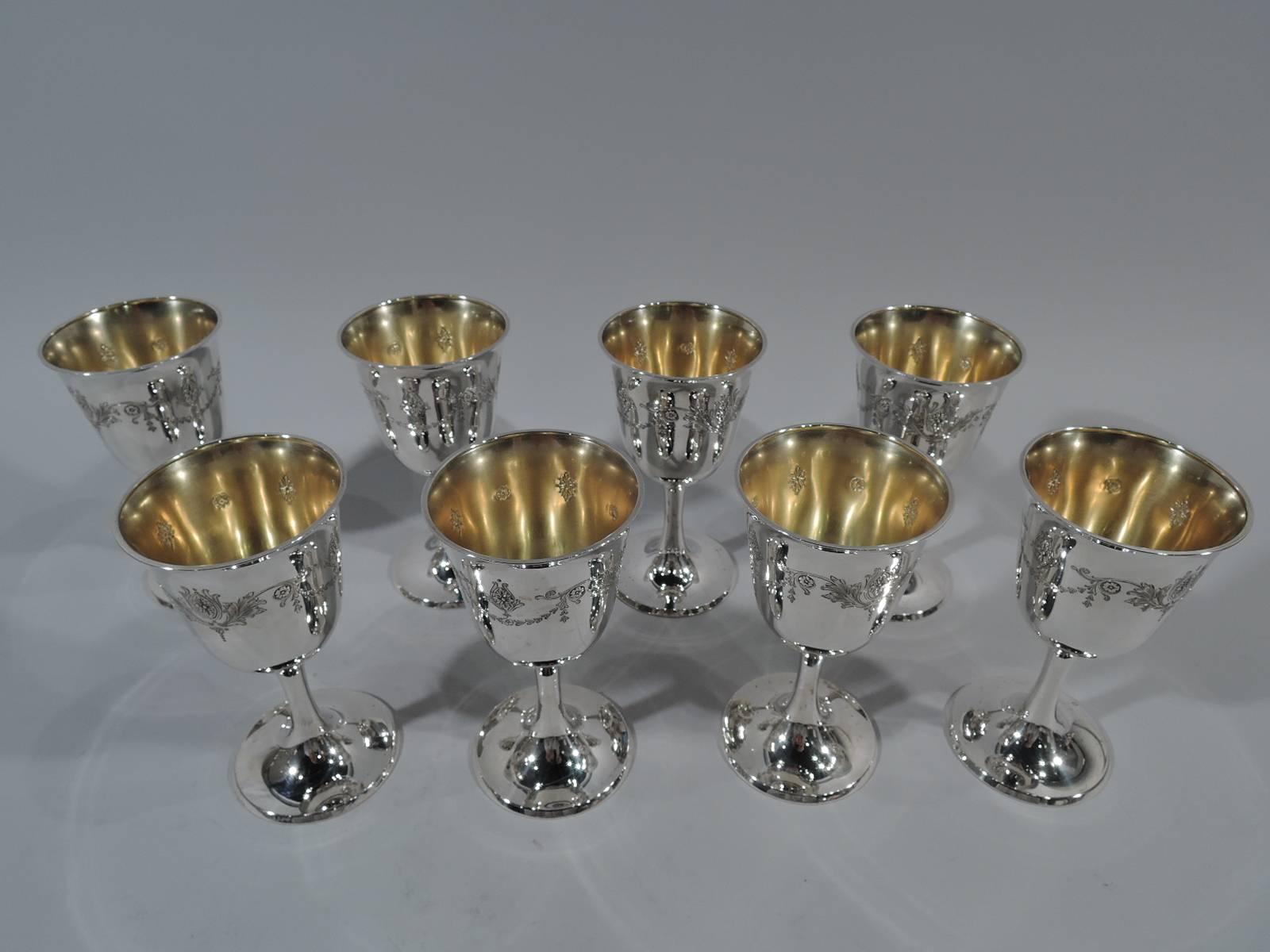 Set of eight Edwardian sterling silver goblets. Made by Whiting in New York in 1916. Each: Bell bowl with flared rim, slender stem, and raised foot. Body has chased and repousse garland with paterae, leaves, and flowers. Interior has gilt wash.