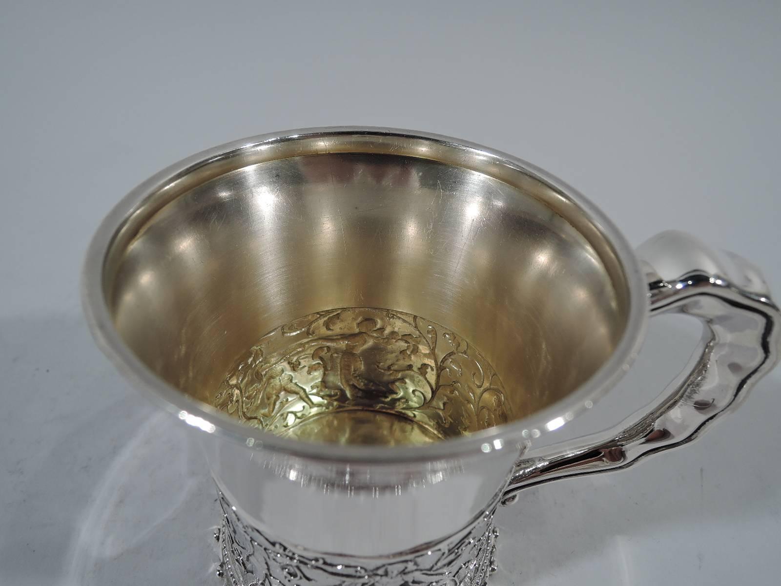 Sterling silver baby cup. Made by Gorham in Providence, ca 1890. Flared rim, notched stroll handle, and studded base. At bottom is chased (and chaste) troubadour scene: Men in tunics and hose and women in gowns and wimples dance amidst leafing