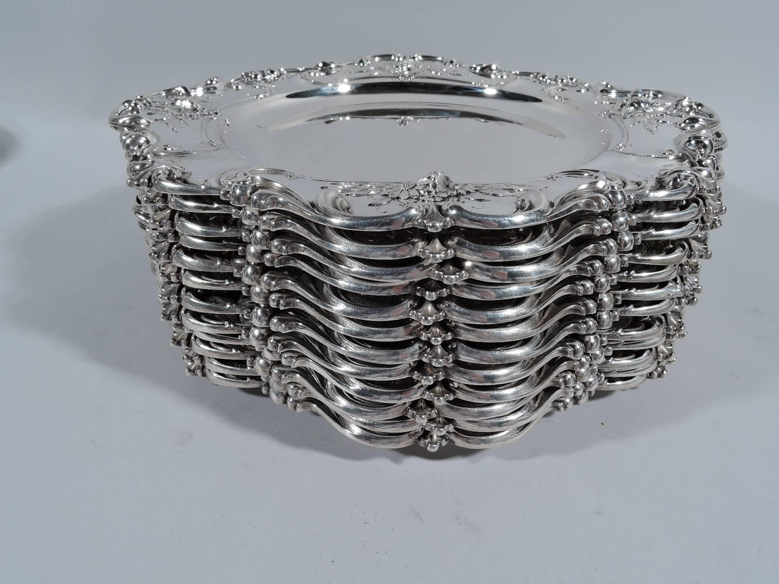 Set of 12 sterling silver chargers. Made by Redlich in New York, circa 1890. Each: plain well and fancy rim with chased and applied scrolls and daisies. A great high-low design that uses a precious metal to represent the humble flower. Hallmark