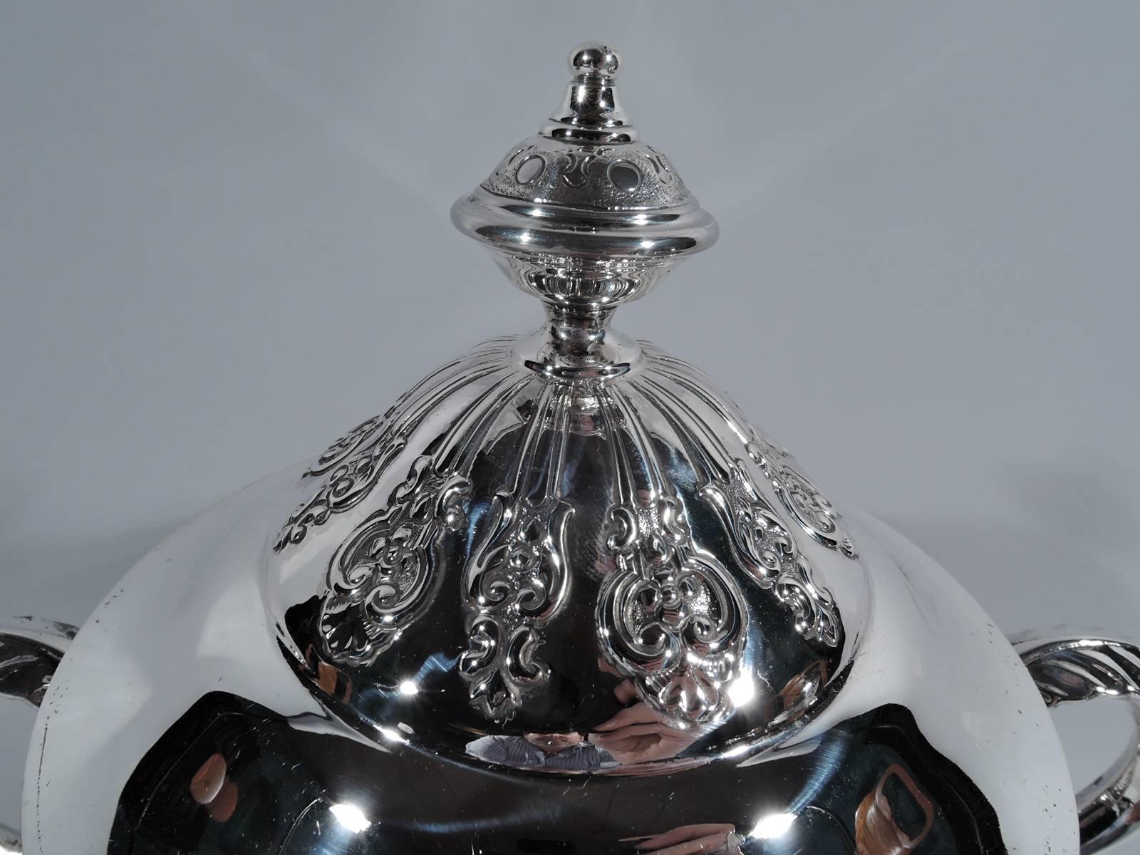 George V sterling silver trophy cup. Made by Fenton Bros in Sheffield in 1921. Bowl has straight sides and curved bottom and rests on domed foot. Leaf-capped double-scroll side handles. Domed cover with ornamental finial. Chased and repousse