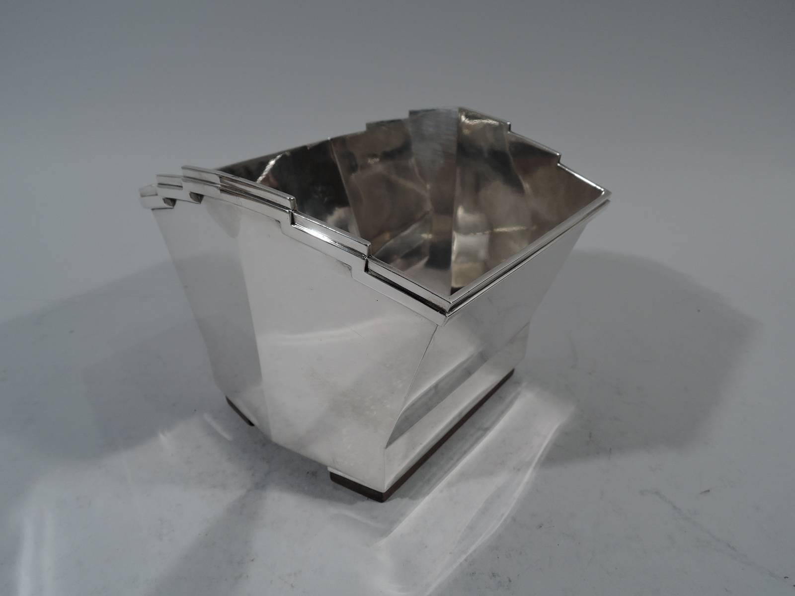 Art Deco 950 silver ice bucket. Made by Tetard Frères in Paris, circa 1930. Trapezoidal with applied rim and two rectangular supports mounted to stained-wood. Sides gently convex with fashionable skyscraper motif. Fully marked with Minerva head and