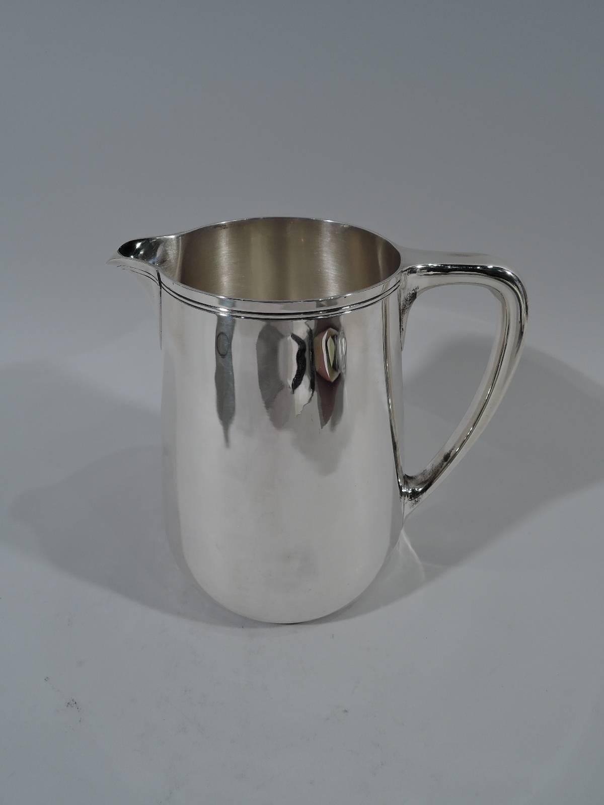 Sterling silver water pitcher. Made by Tiffany & Co. in New York. Upward tapering sides, scrolled bracket handle, and v-spout. Softened Modernism with spare incised banding wrapping around rim and spout. Hallmark includes pattern no. 22343 and