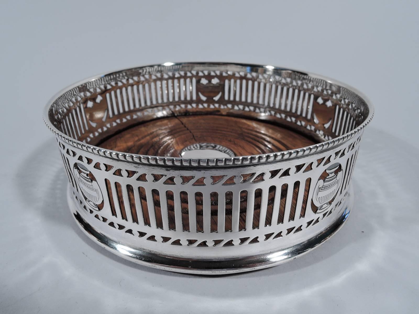 George V sterling silver wine bottle coaster. Made by Harry Freeman in London 1912. Pierced lines and rinceaux, open ovals inset with amphorae, and beaded rim. Stained and felt-lined wood well. Hallmarked.