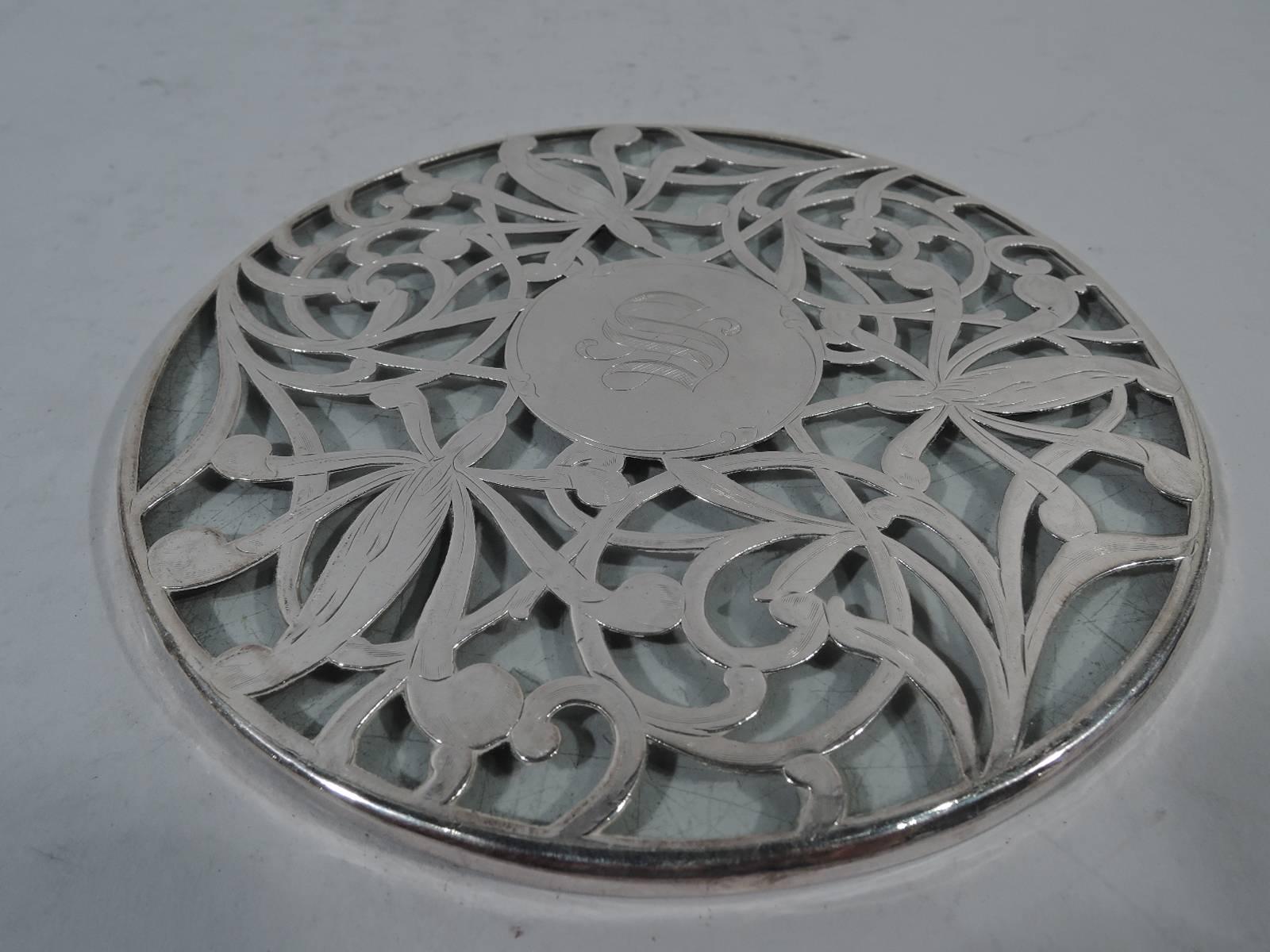 Art Nouveau clear glass trivet with silver overlay. Circular with overlaid semi-abstract flowers and intertwined tendrils. Shaded block monogram. Hallmarked sterling.