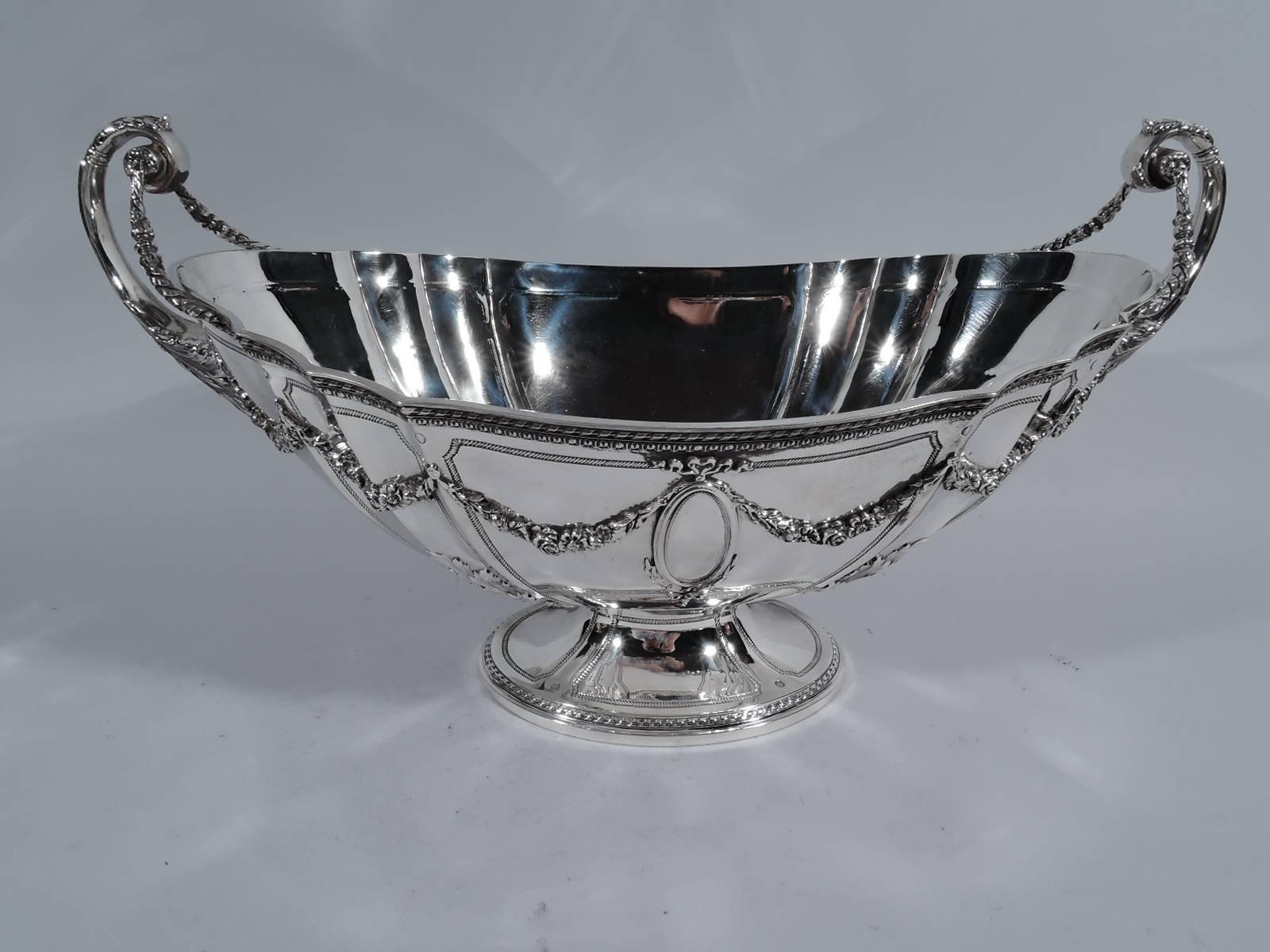 Neoclassical sterling silver centrepiece bowl on plateau. Made by Bailey, Banks and Biddle in Philadelphia, circa 1910. Bowl: Ovoid with curved and fluted sides and raised foot. Leaf-mounted and capped flying scroll end handles terminating in