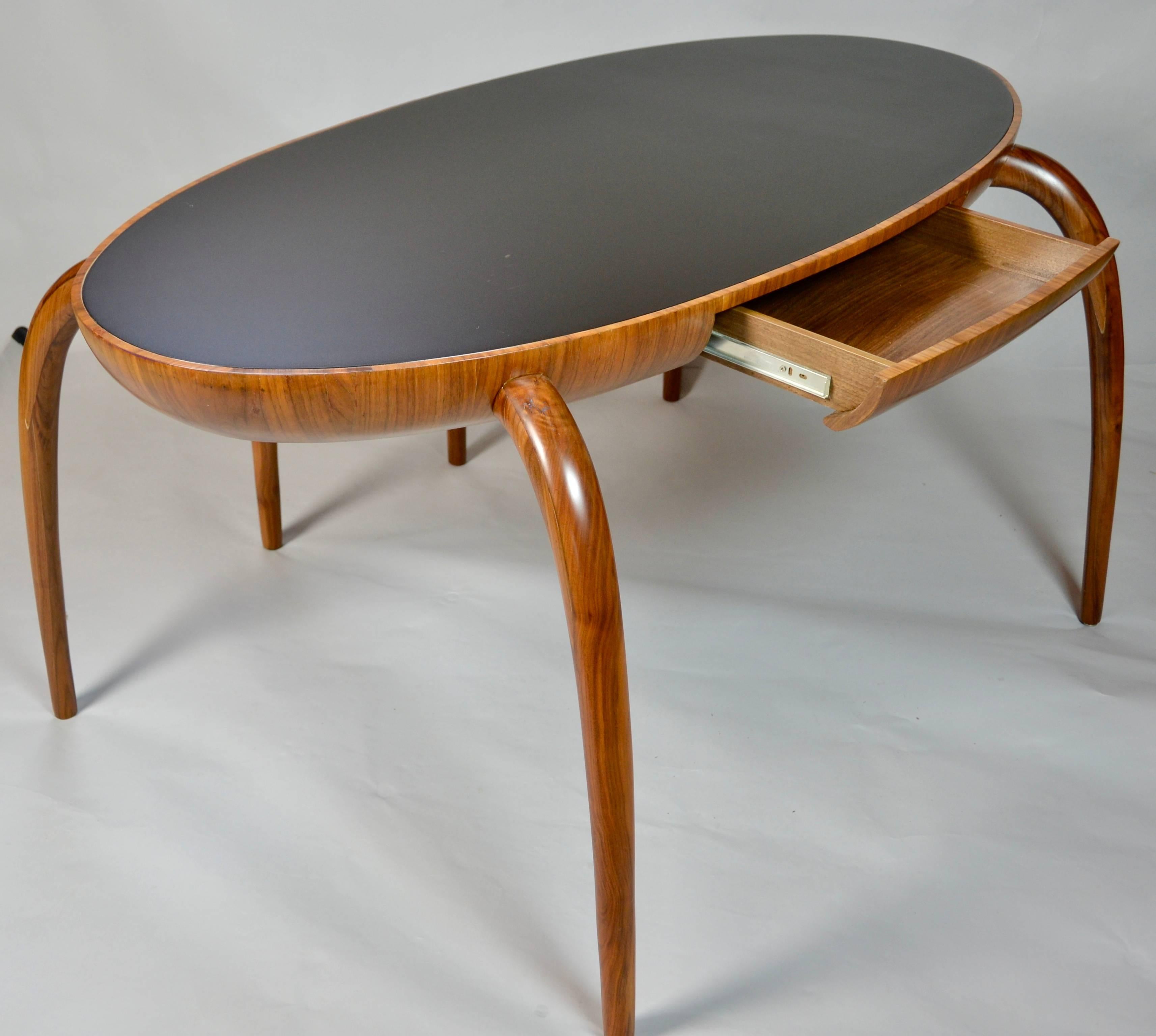 Unusual spider legged oval top writing desk with a single inset drawer. 
Handcrafted and laminated in a walnut veneer with hand shaped removable legs and an inset black glass top.
The desk is in excellent condition.