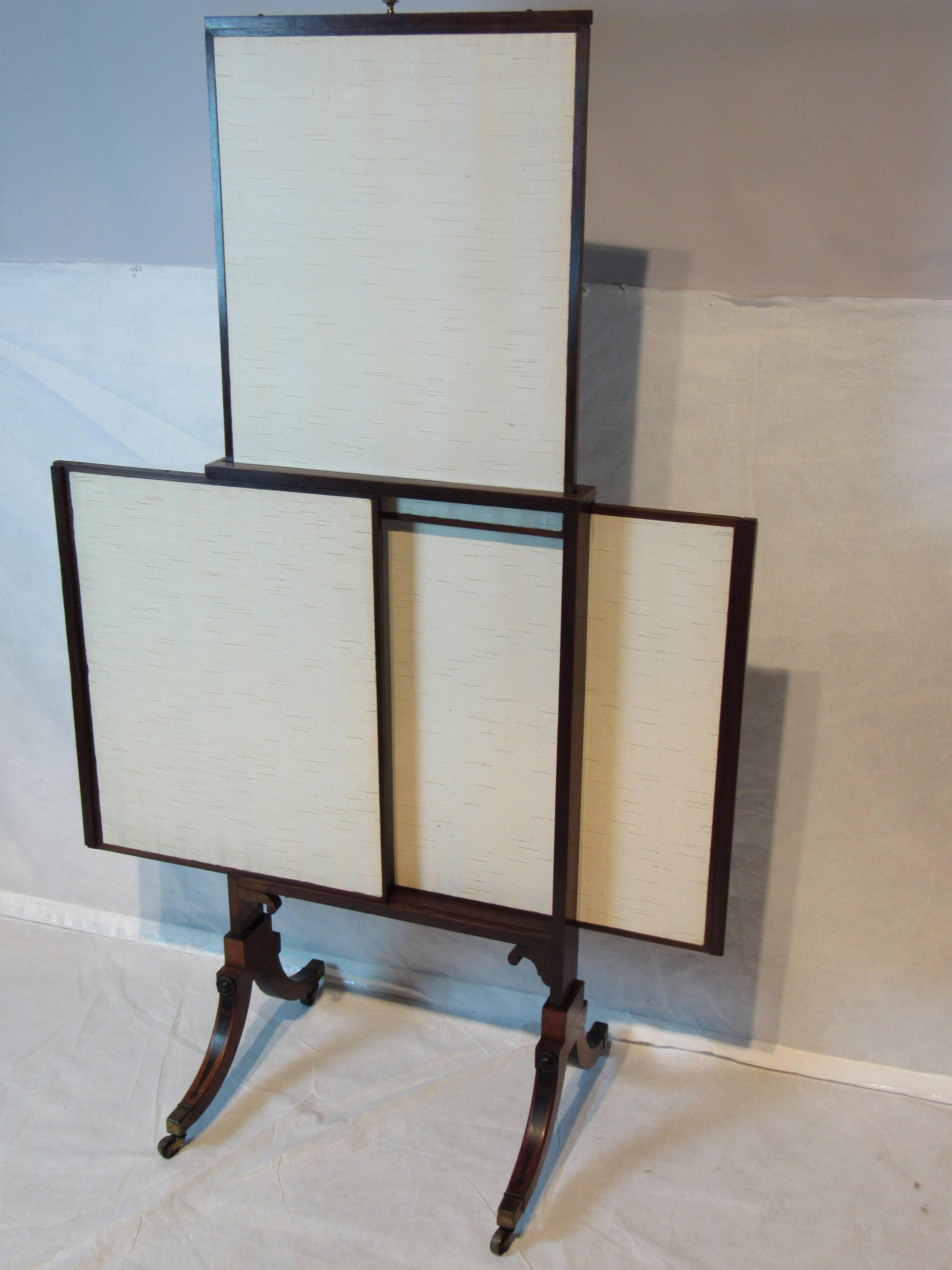 Unusual American mahogany extendable fireplace screen in the style of Thomas Sheraton. 
The classically styled mahogany frame with ebonized inlays hold three raw linen upholstered panels that are adjustable. 
The rolling frame rests on brass sabots