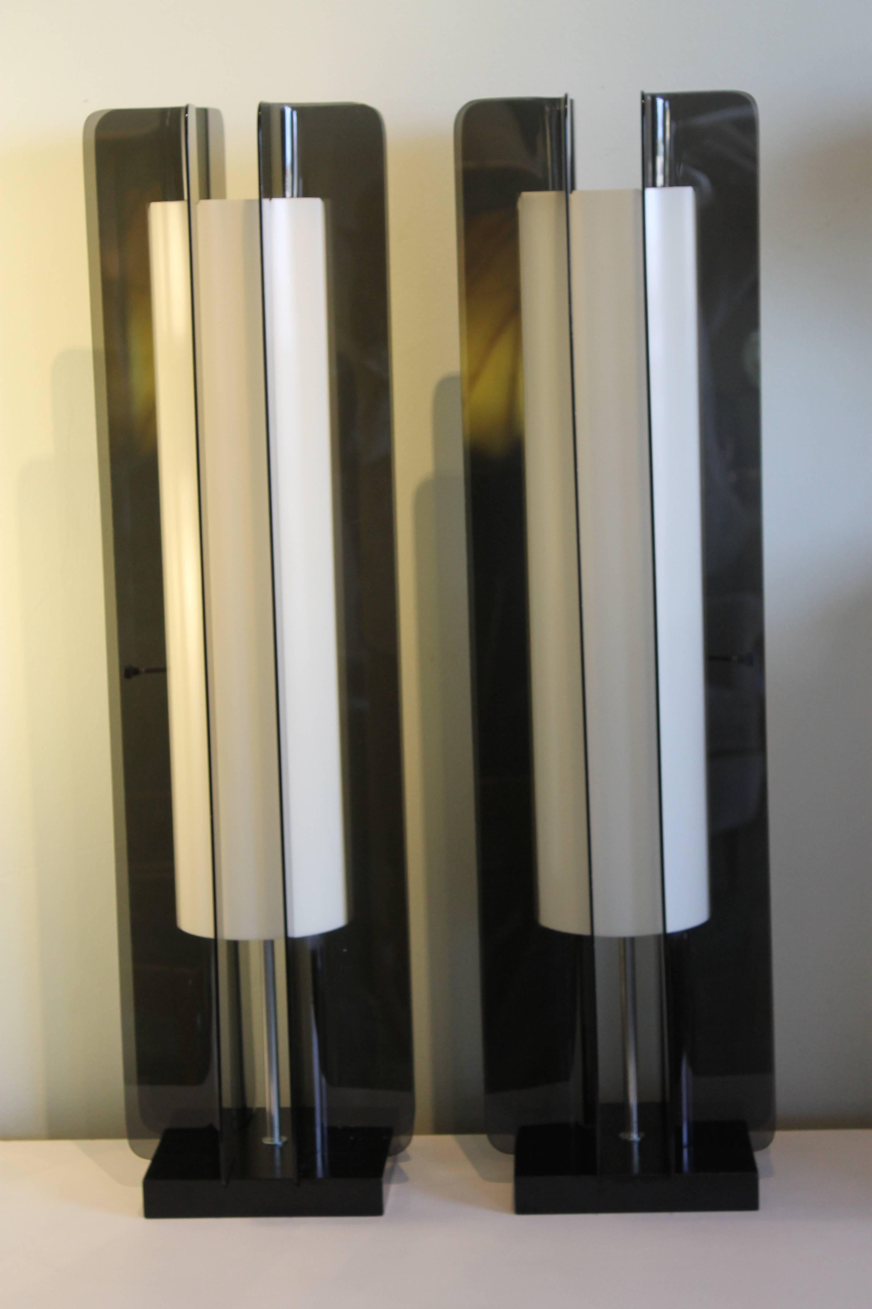 Matched pair of circa 1970s tall table lamps. White plastic cylinders are surrounded by four smoke colored clear Lucite walls and mounted on black painted wooden bases. Lamps are newly refurbished and rewired with three-way switches. Total height is