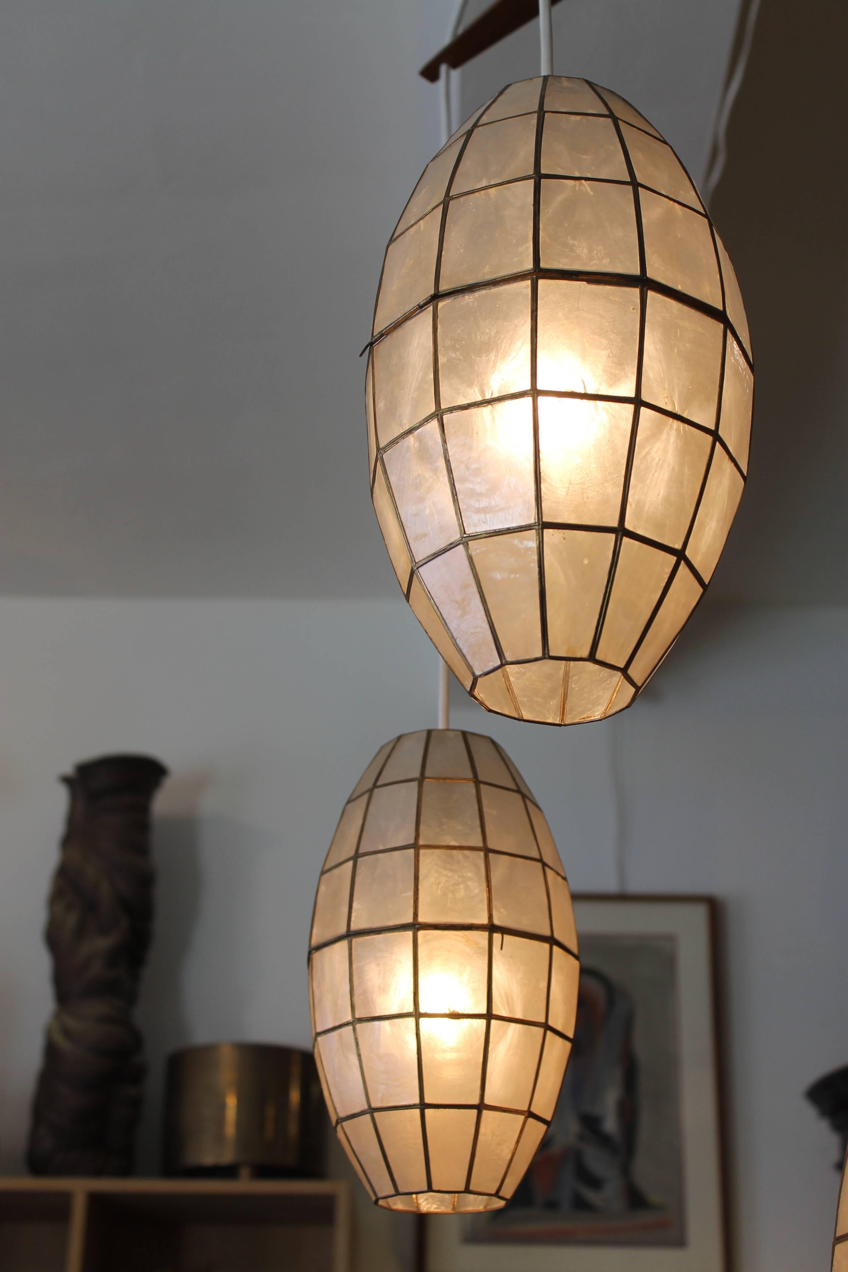 A circa 1960s hanging fixture with three cigar shaped globes made of leaded capiz shell, held apart by a solid teak three-pointed spacer. Shades vary in size, the lengths being 20