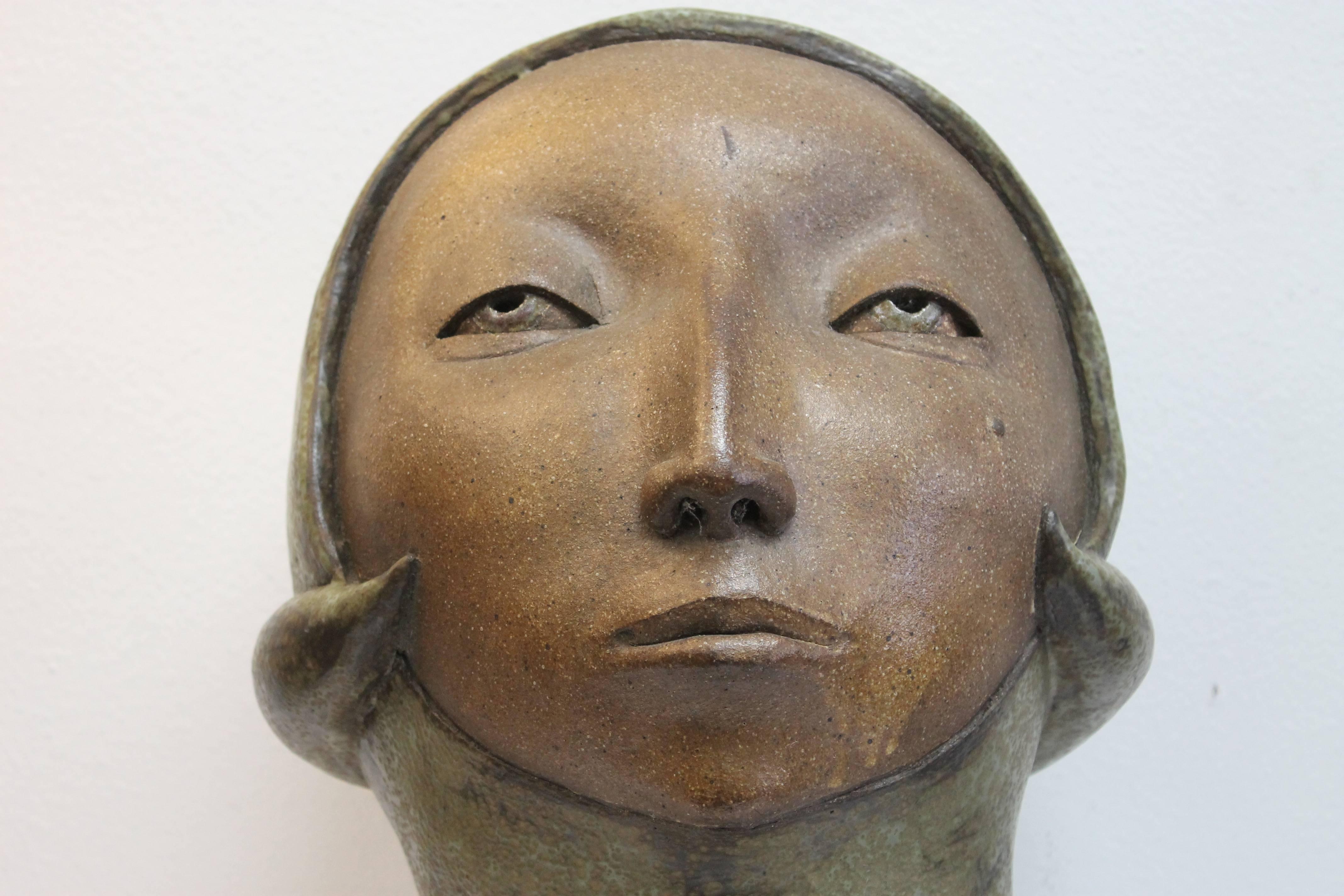 A large-scale hand built stoneware sculpture with futuristic head covering. Clay body is dark brown with a matte green glaze. The woman's face is quite intriguing in its multi-ethnic features and the serene and hypnotic Metropolis expression. We're