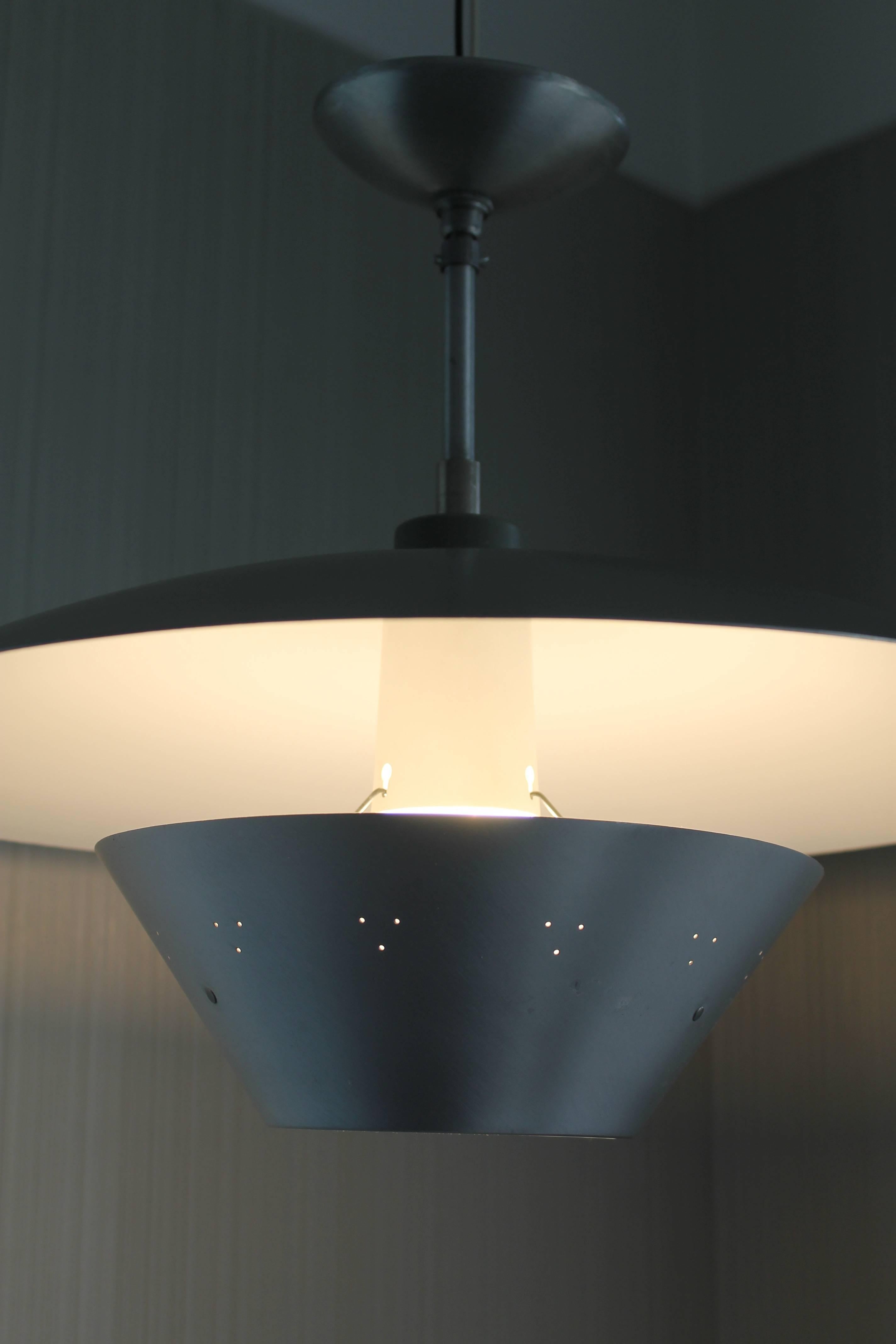 A spun aluminium saucer shaped hanging fixture, circa 1950s. The pierced lower dish directs light up into the (white) underside of the large saucer shade. Upper surface of the saucer is painted grey. Fixture includes the original spun aluminium