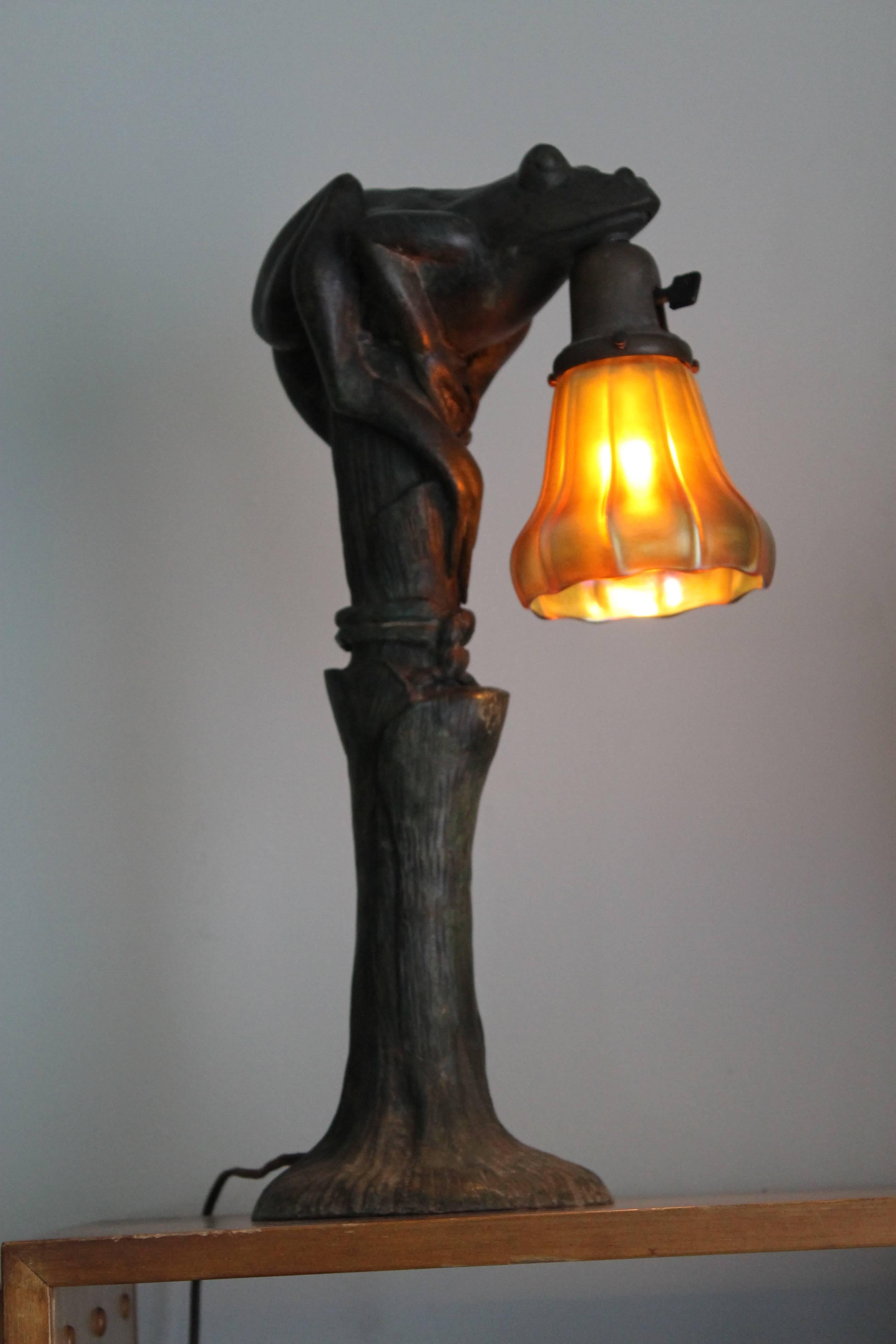 Art Nouveau figural bronze frog lamp with Steuben shade. A circa early 1900's cast bronze frog lamp fitted with a signed Steuben Aurene glass blossom shaped shade. The lamp stands 20" tall. The Steuben shade is 5"long and 5" wide.