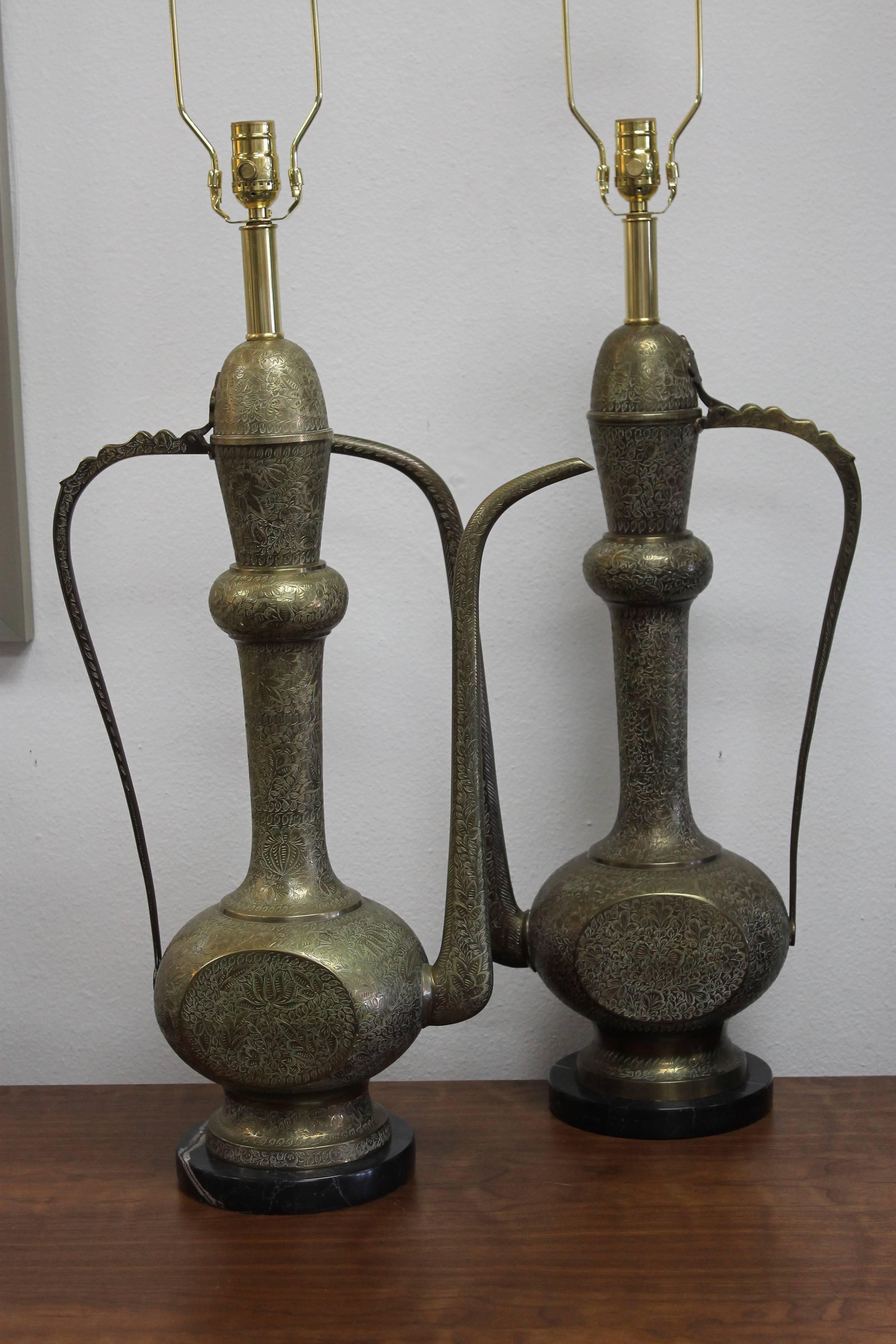 Pair of custom lamps. Engraved brass carafes we converted to table lamps. Black/white marble bases. We took the top portion of the carafes and made them the finials. They are similar but, etching is different on both of these carafes (no two are