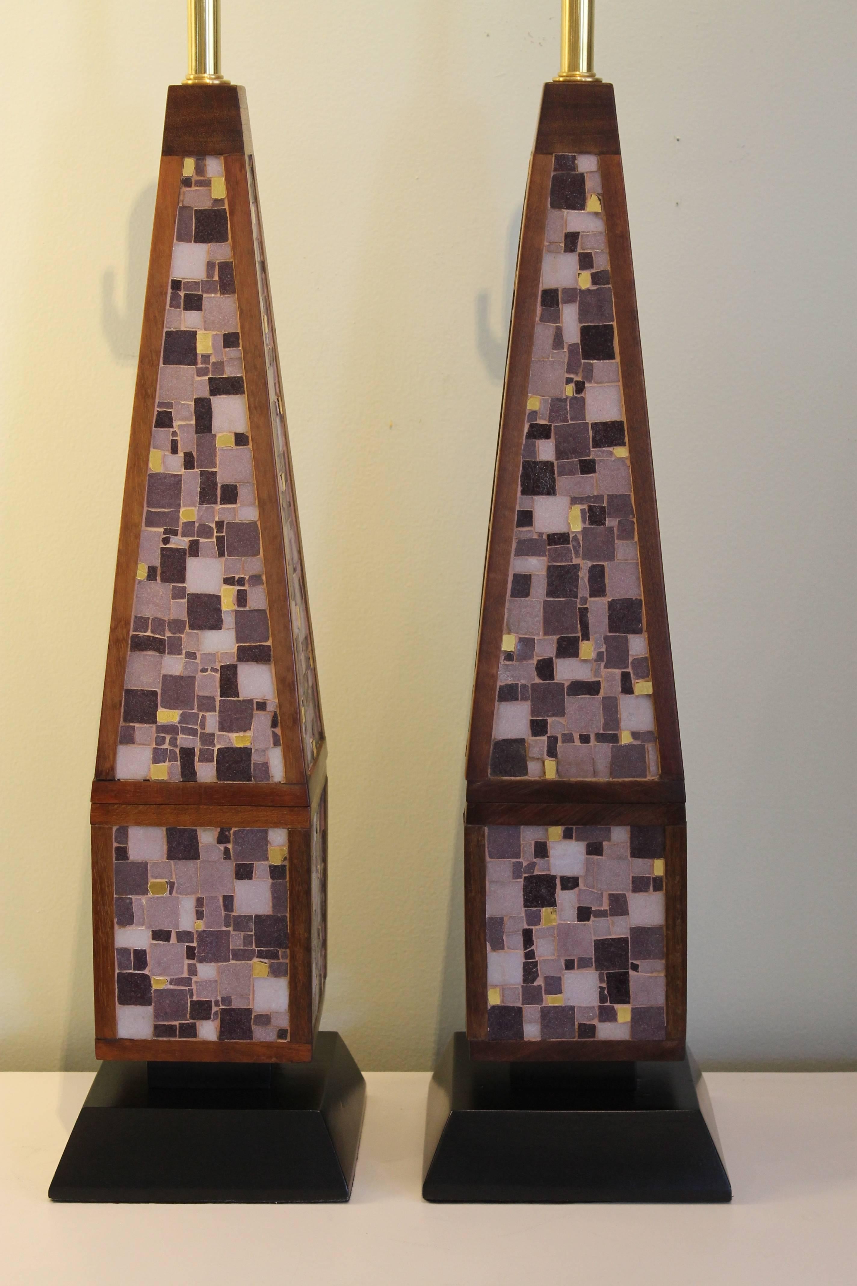 A matched pair of large solid mahogany obelisk shaped lamps inlaid with vitreous glass tiles. Tiles are all individually cut and laid by hand and are in soft shades of lavender with bright gold accents. Bases are black painted mahogany. These