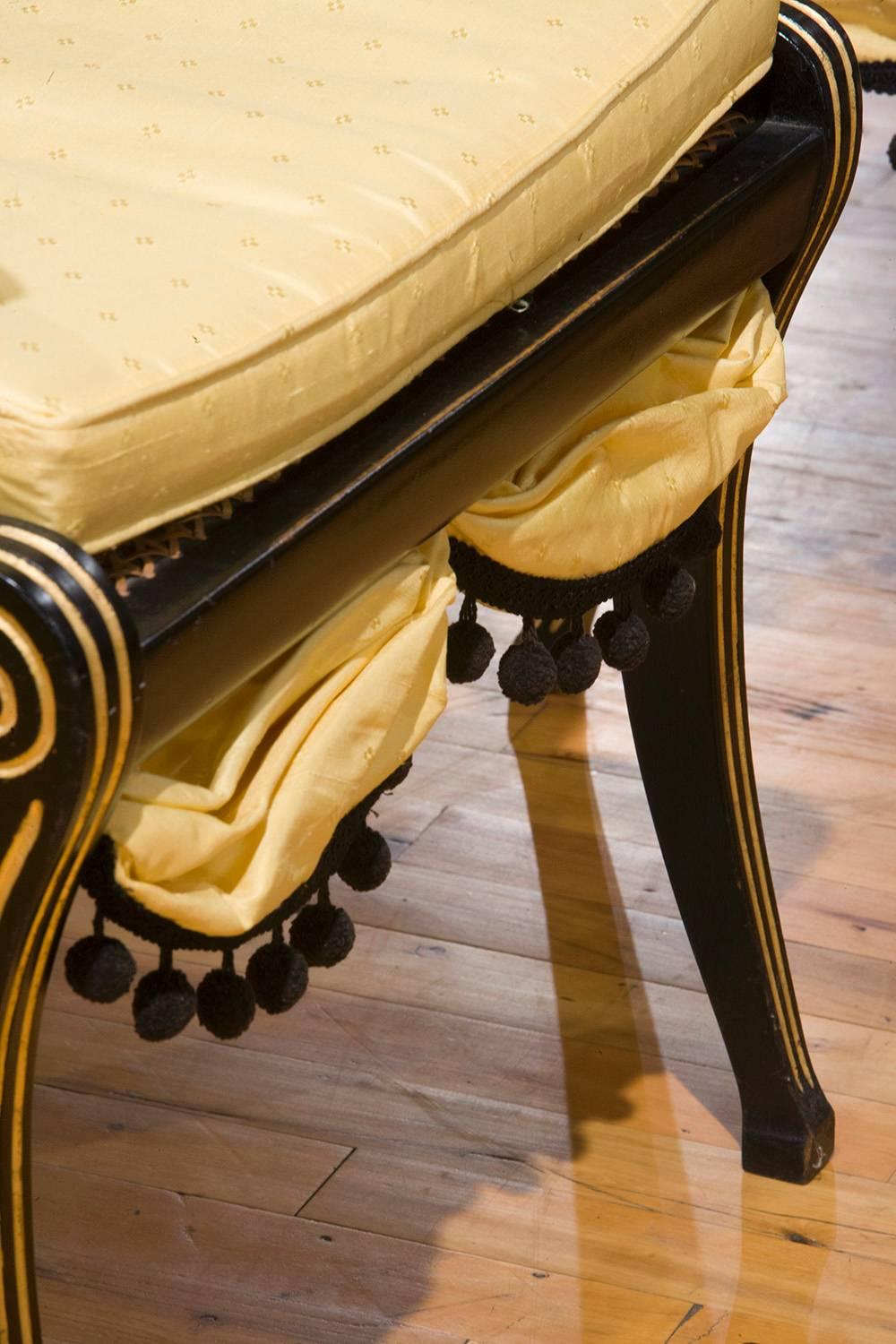 These 19th Century Regency Ebonized Beech open armchairs, with sabre legs. The back support has inlaid gold gilt. Connecting to curved support rails, inlaid with gold gilt bands, leading to the sabre legs. They have matching seat skirts with ball