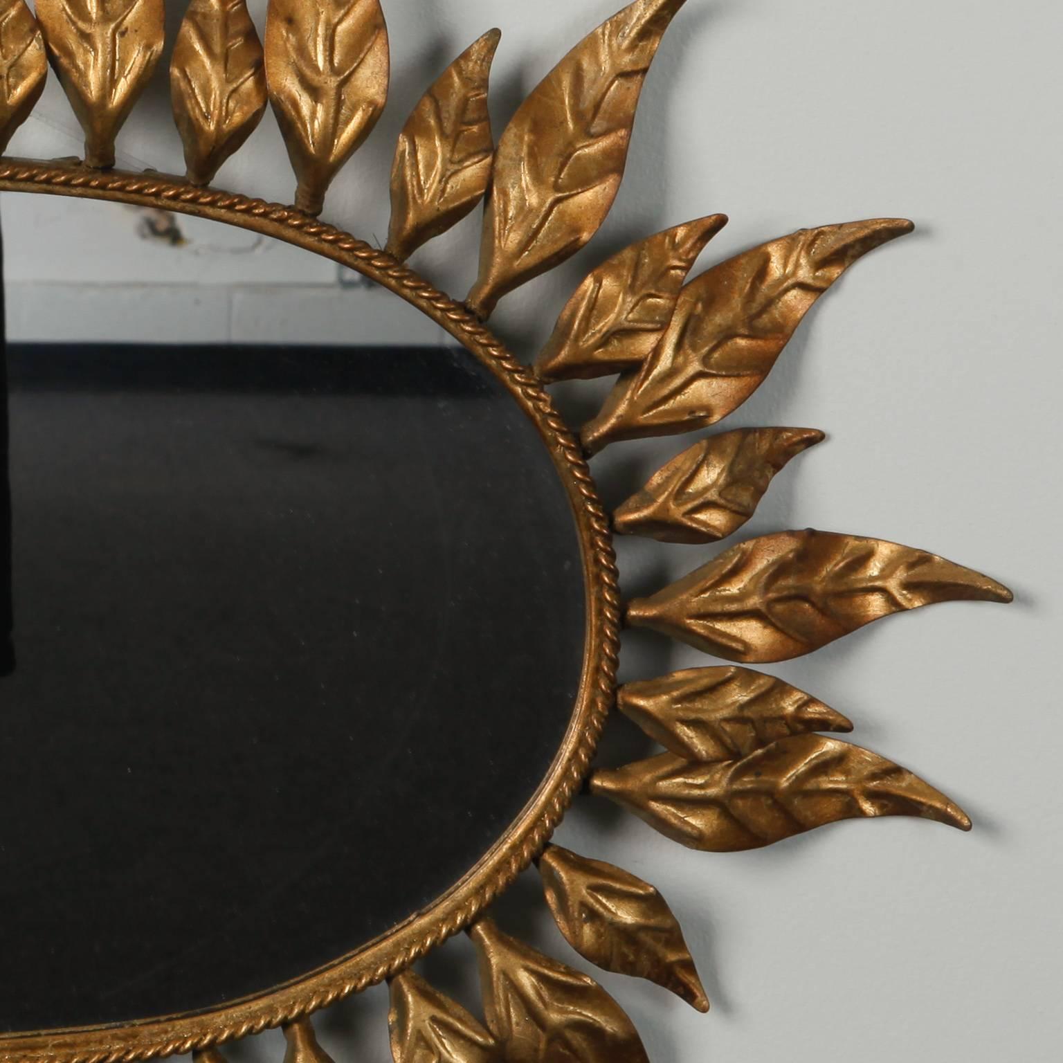 Oval mirror with pressed gold tone metal leaf form rays forming a sunburst frame, circa 1960s. Twisted, rope form inner border. 
