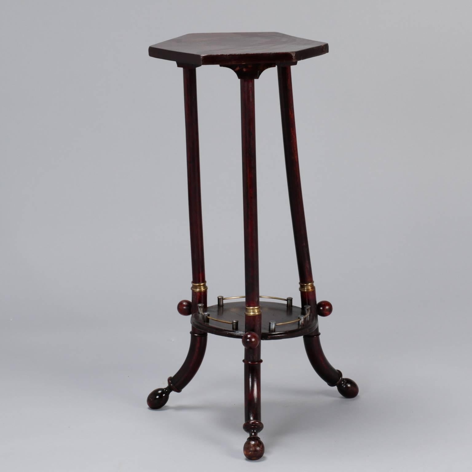 Slender Thonet side table in dark stained wood with three legs, lower shelf with brass gallery and trim and a six sided table top, circa 1930s.
     